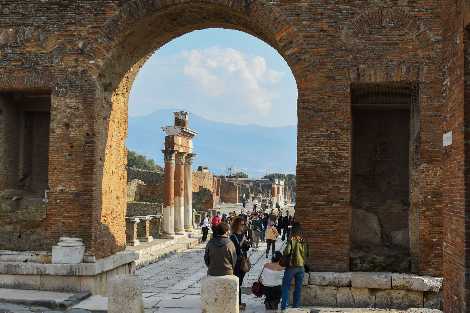 Ancient stone ruins and archways at Pompeii with tourists walking through the historic site.