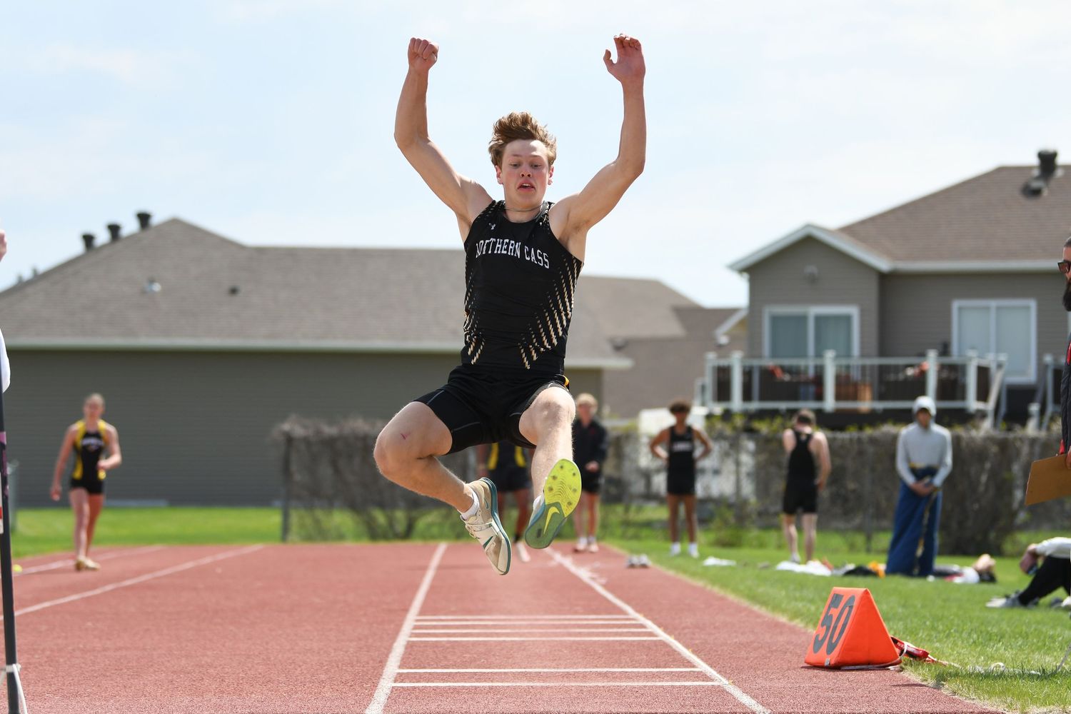 Track athlete soars over sand pit during long jump competition at outdoor meet.