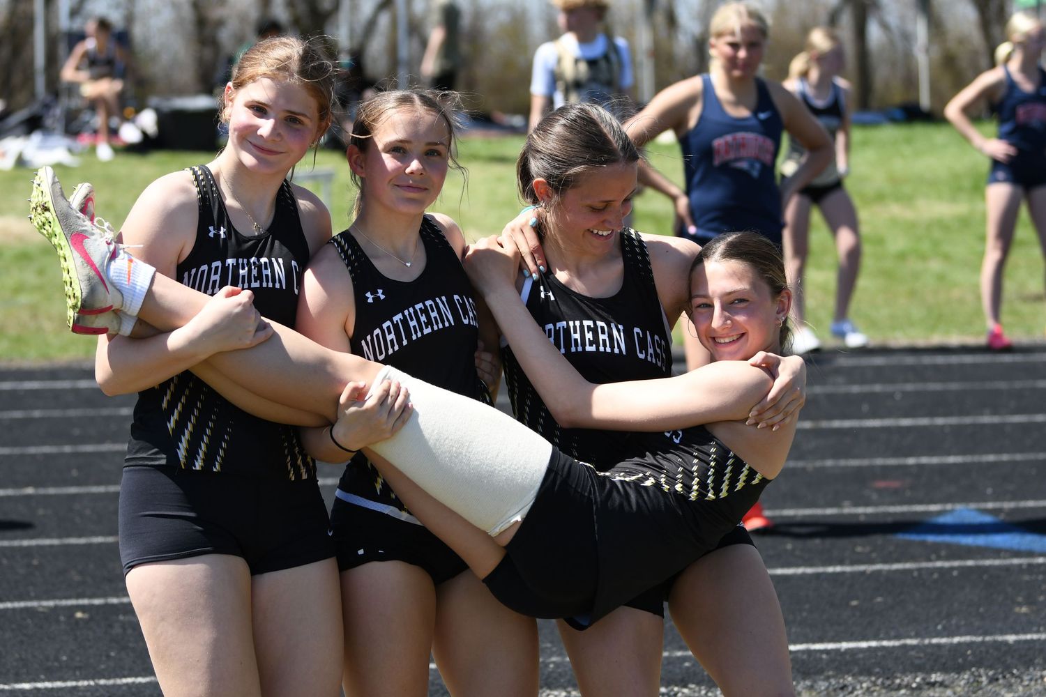 Athletes in black uniforms celebrating together on a track field.
