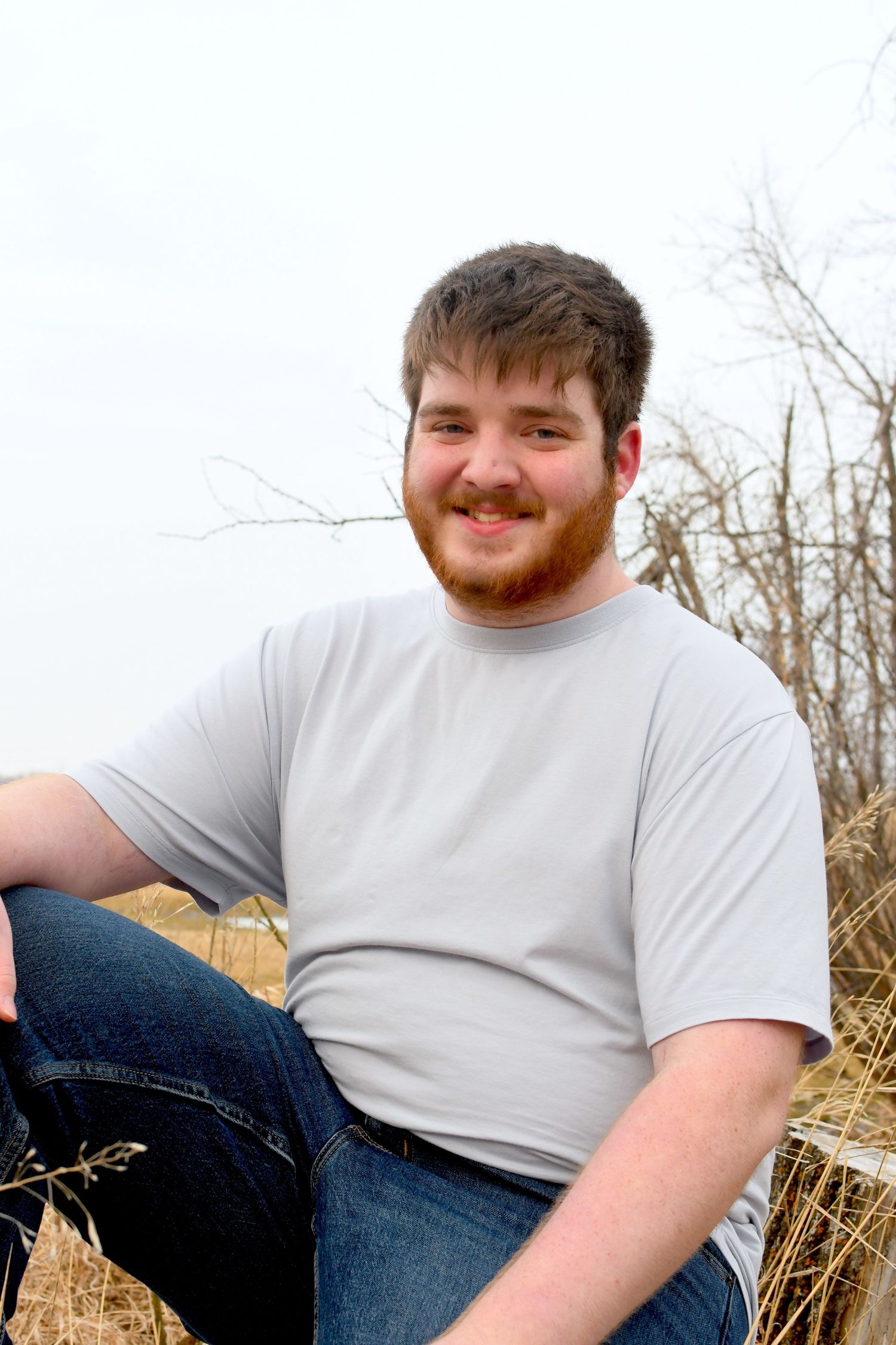 Casual outdoor portrait in natural setting with tall grass and trees.