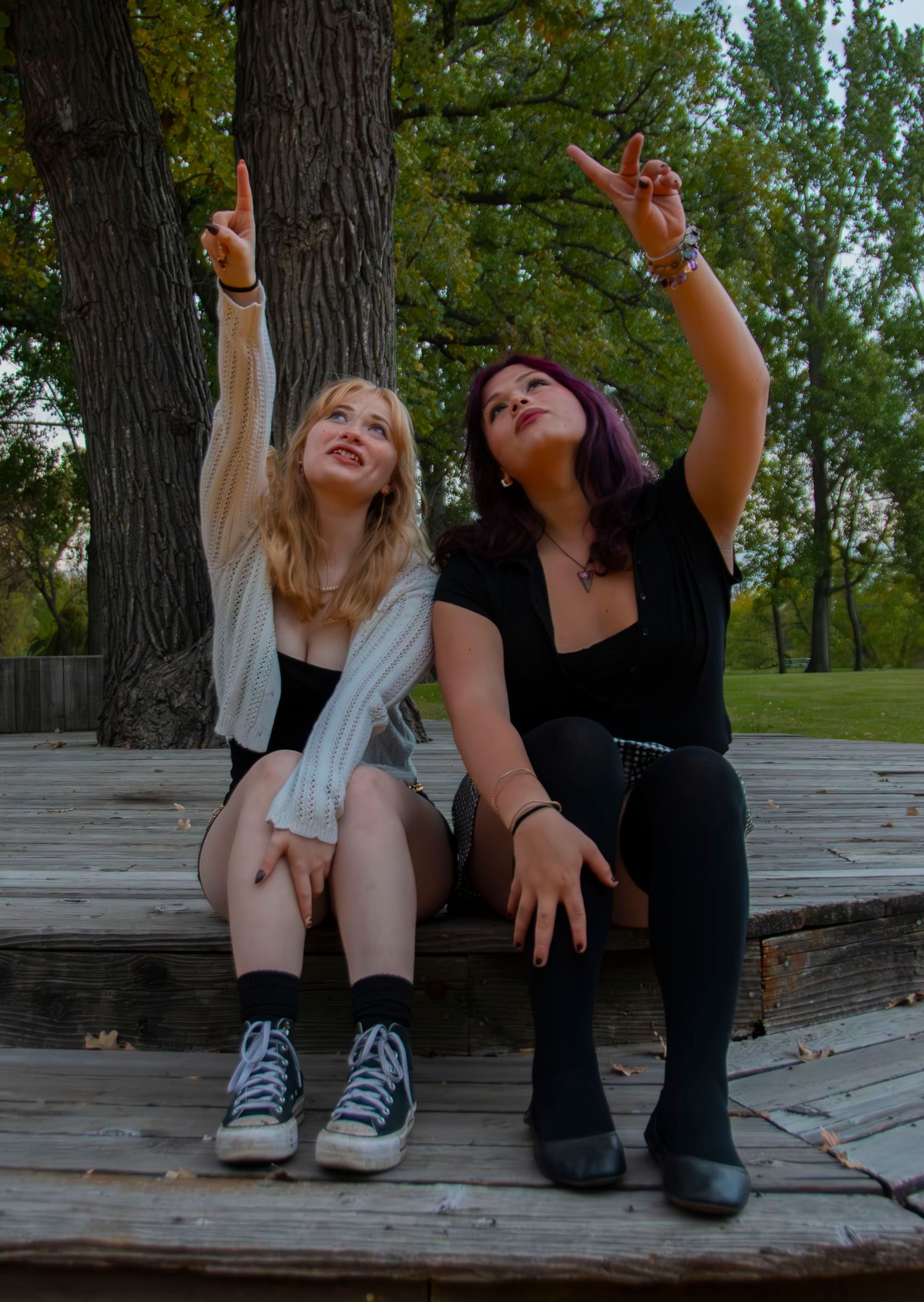 Two friends sitting on wooden steps outdoors, laughing and raising their arms in a joyful moment together.