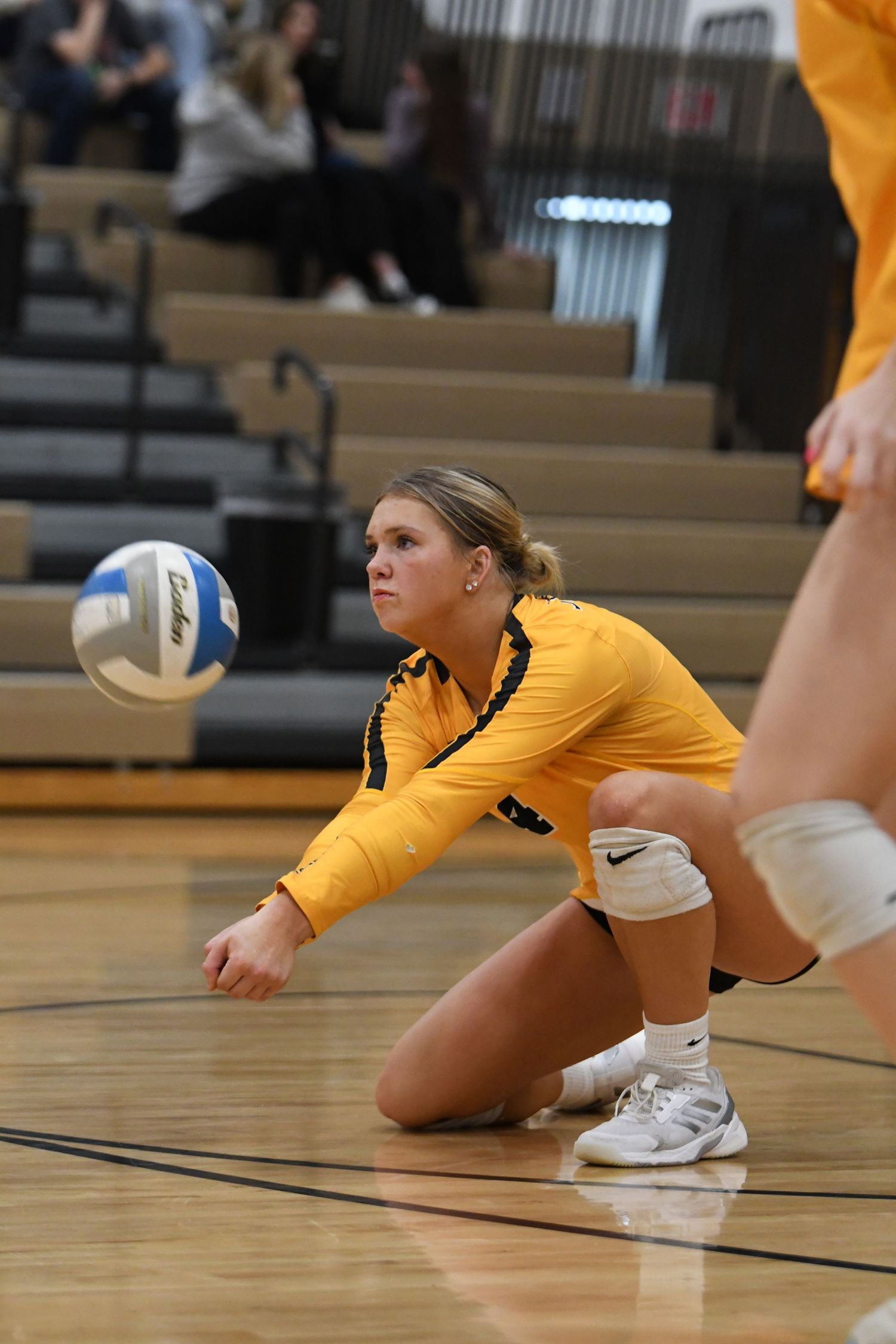 Volleyball player in yellow uniform dives for ball during defensive play.