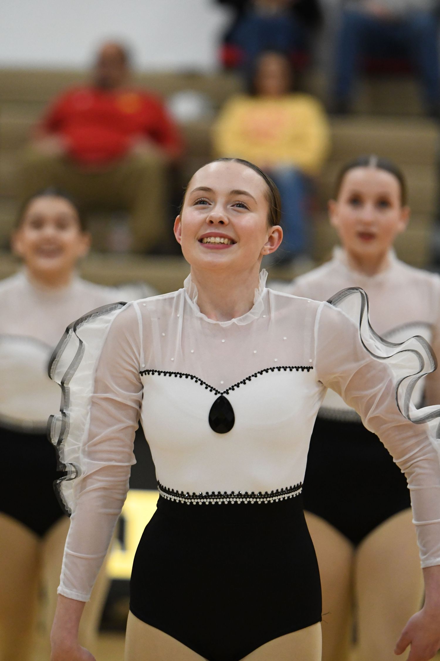 Performer in black and white leotard with sheer sleeves during dance routine in gymnasium.