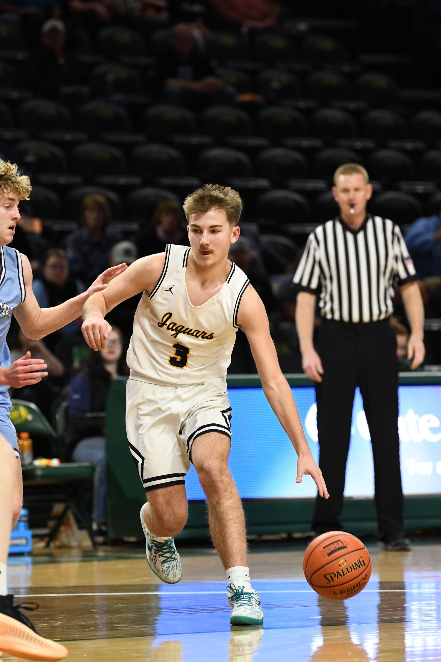 College basketball player dribbles past defender during competitive game on home court.