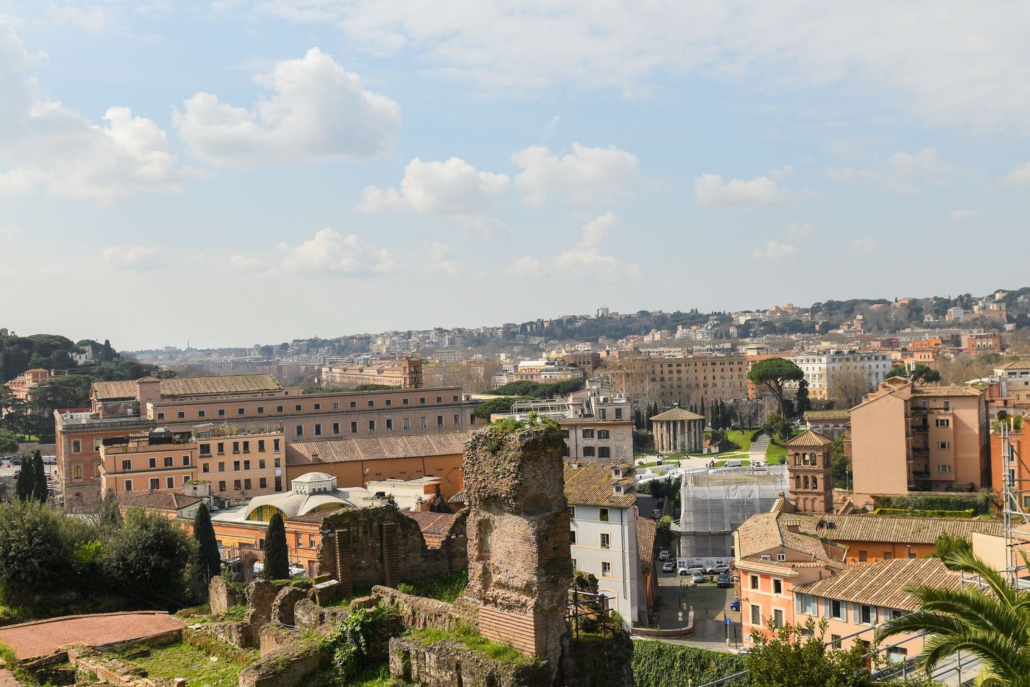 Panoramic view of ancient Roman ruins and modern buildings in Rome's cityscape.