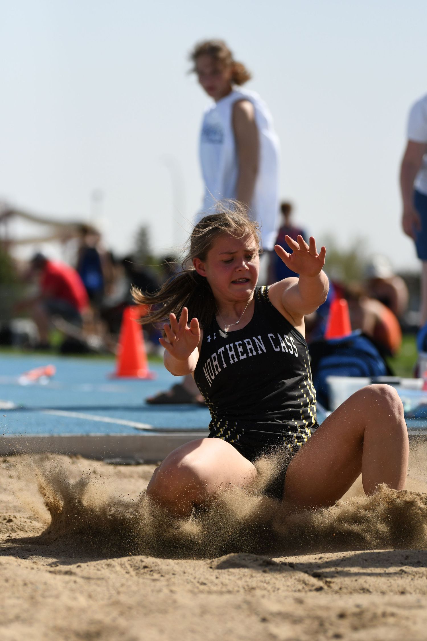Athlete in black uniform lands in sand during long jump competition.