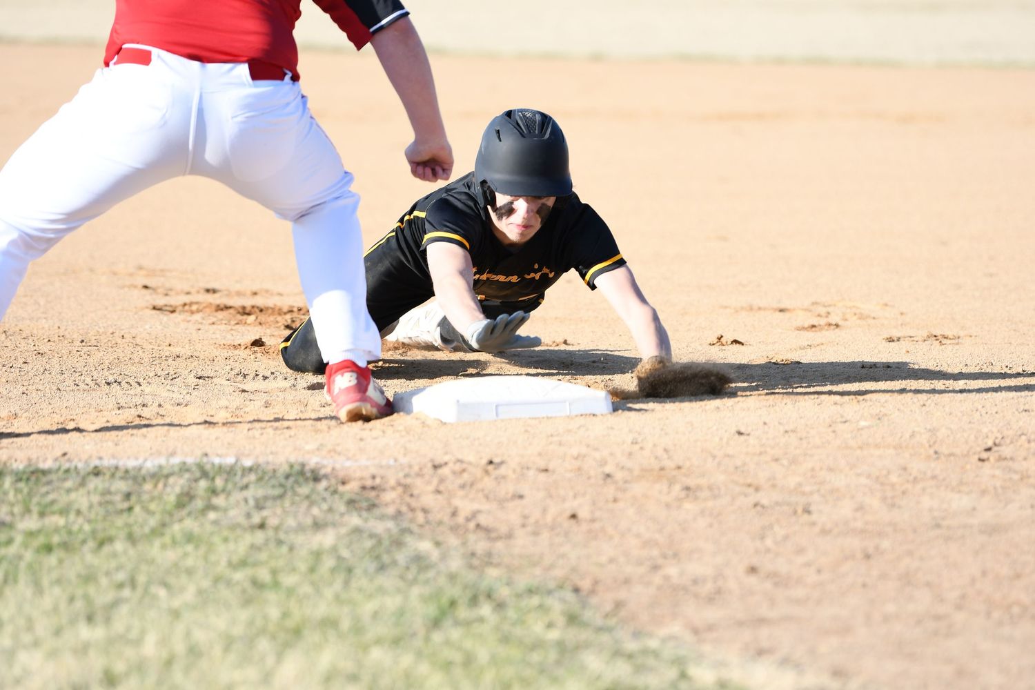Baseball player in black uniform slides into base as opponent in red uniform defends.