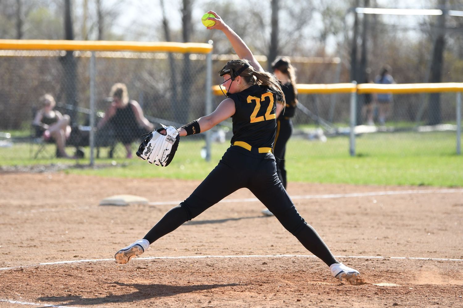 Softball pitcher in black uniform delivering pitch from mound during game.