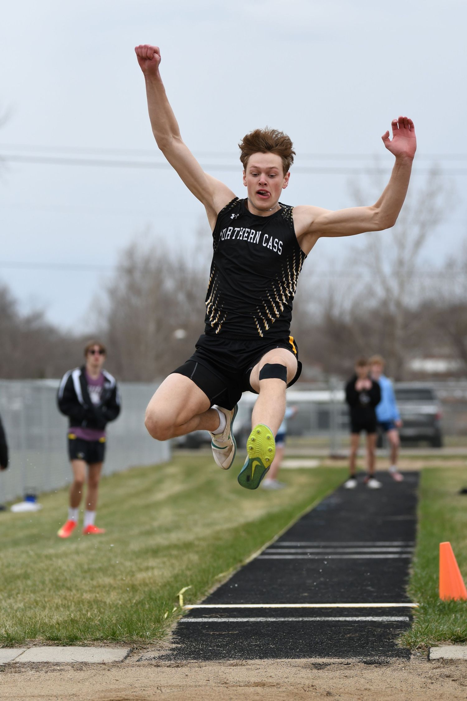 Athlete executes powerful long jump with arms extended at track meet.