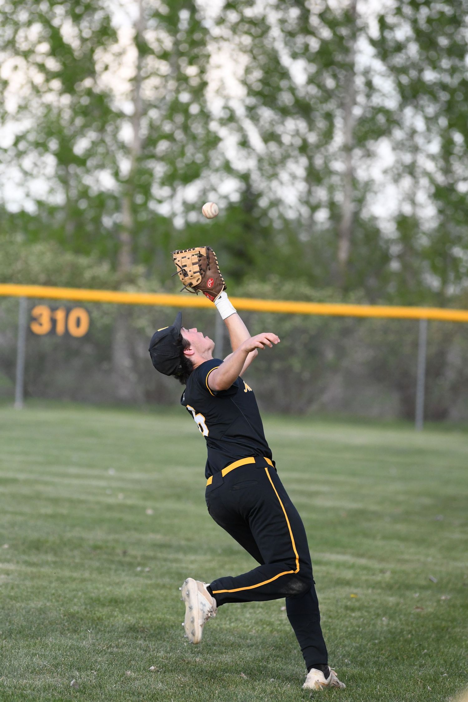 Baseball player in black uniform reaches up to catch a high pop fly in the outfield.