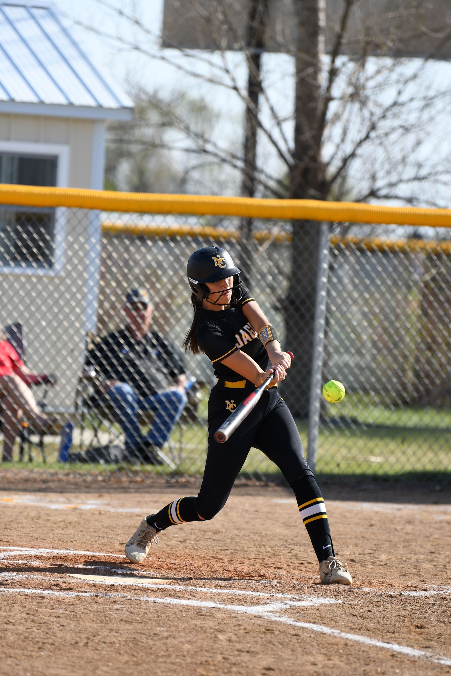 A softball player in a black uniform executes a bunting stance at home plate during a game.