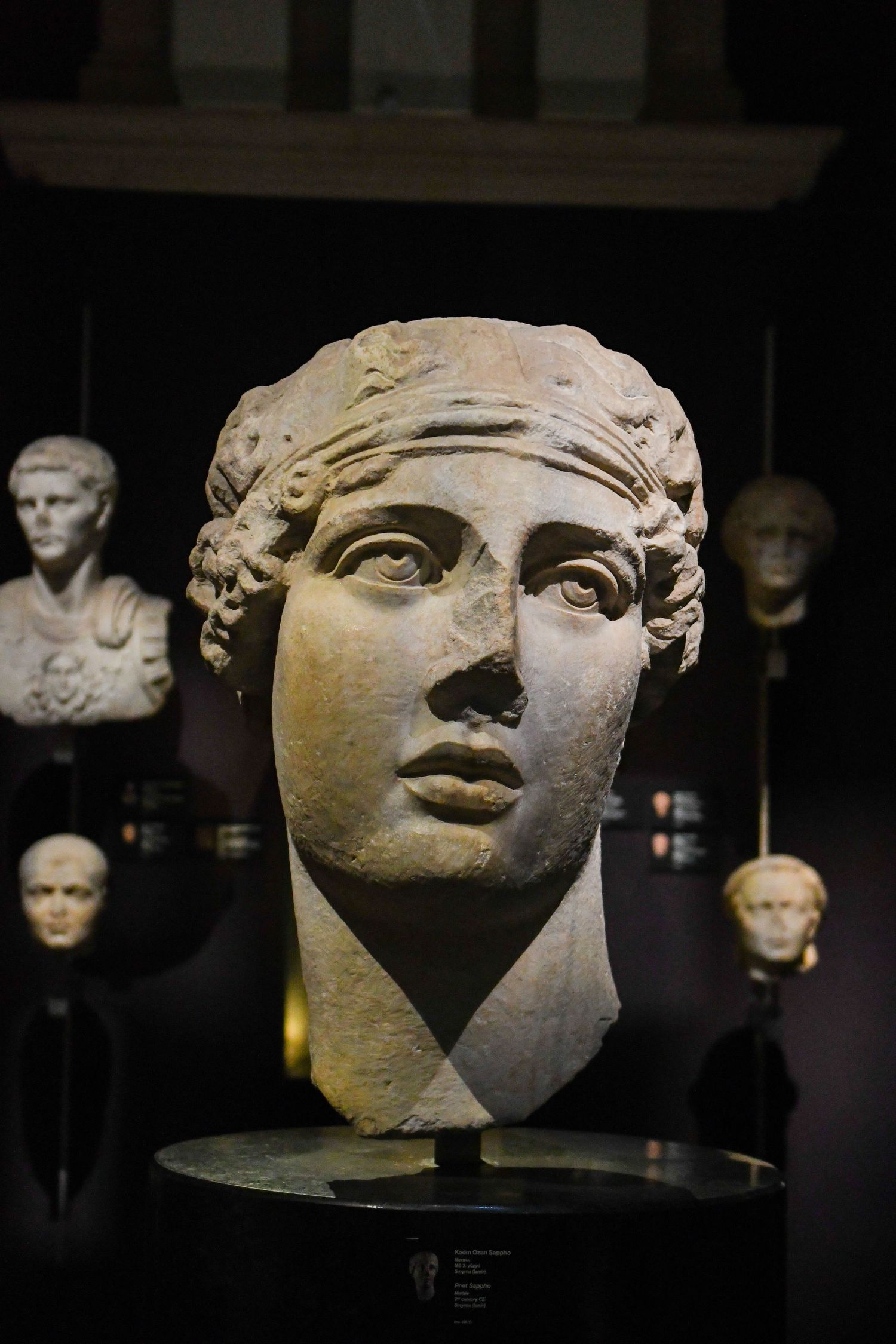 Ancient stone sculptures of faces displayed in a dark museum setting.