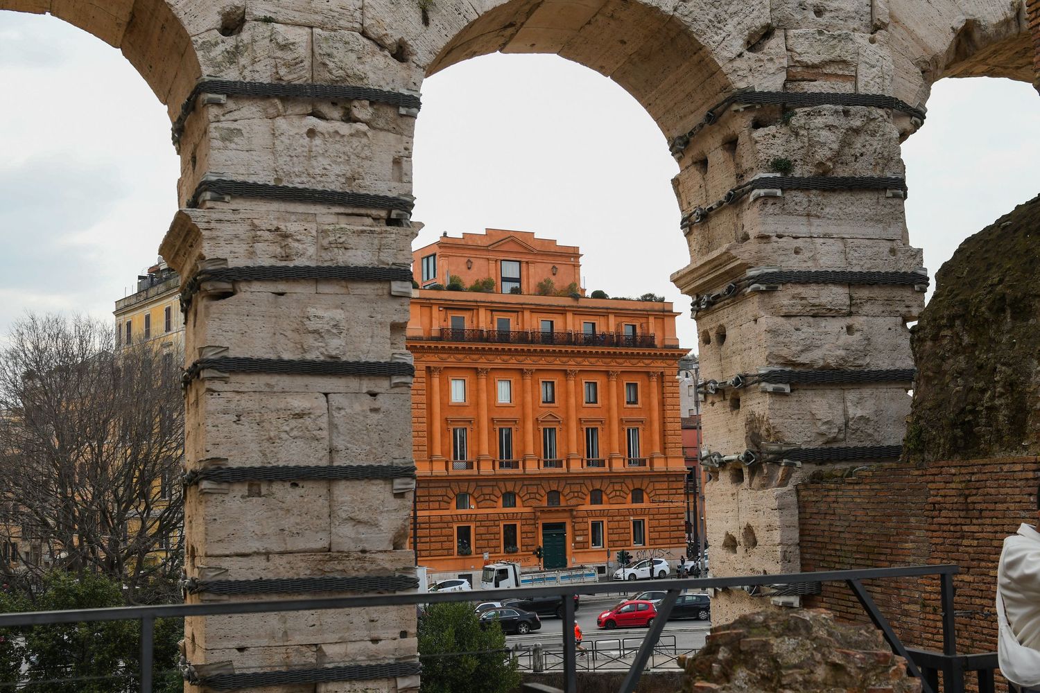 View through ancient stone arches of the Colosseum framing an orange building in Rome's historic center.