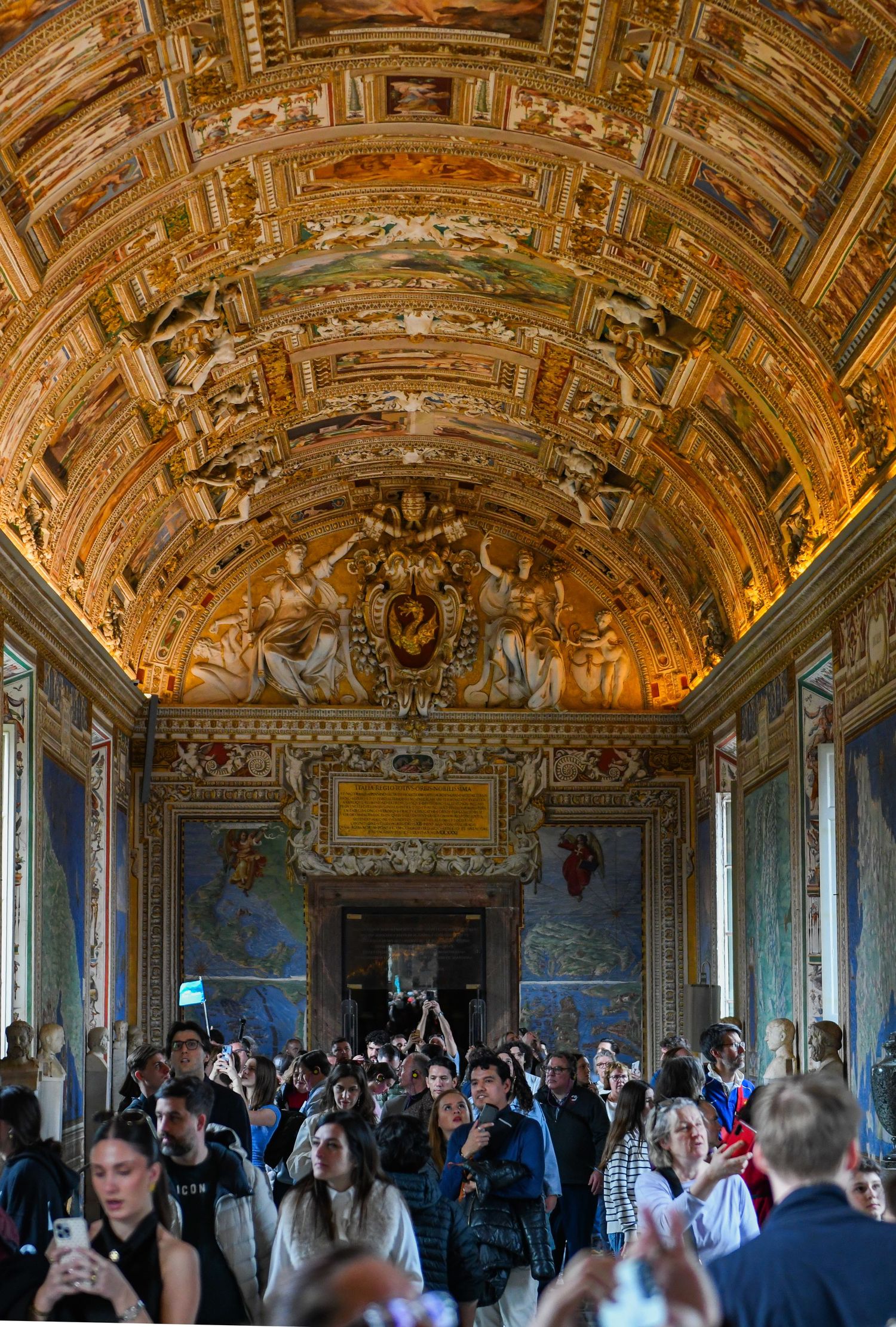 Ornate baroque ceiling with golden frescoes and architectural details in a crowded museum gallery.