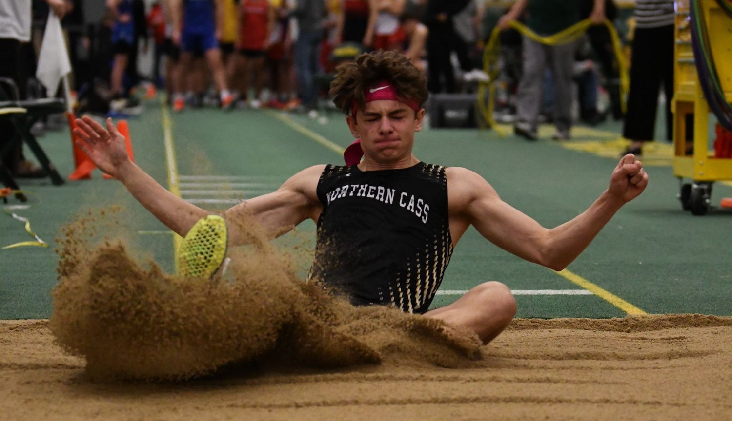 An athlete executes a dramatic long jump into the sand pit during indoor competition.