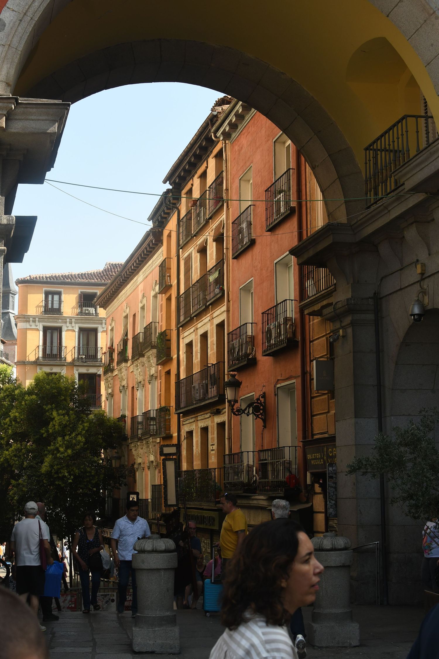 Colorful traditional Spanish buildings with balconies viewed through a stone archway.