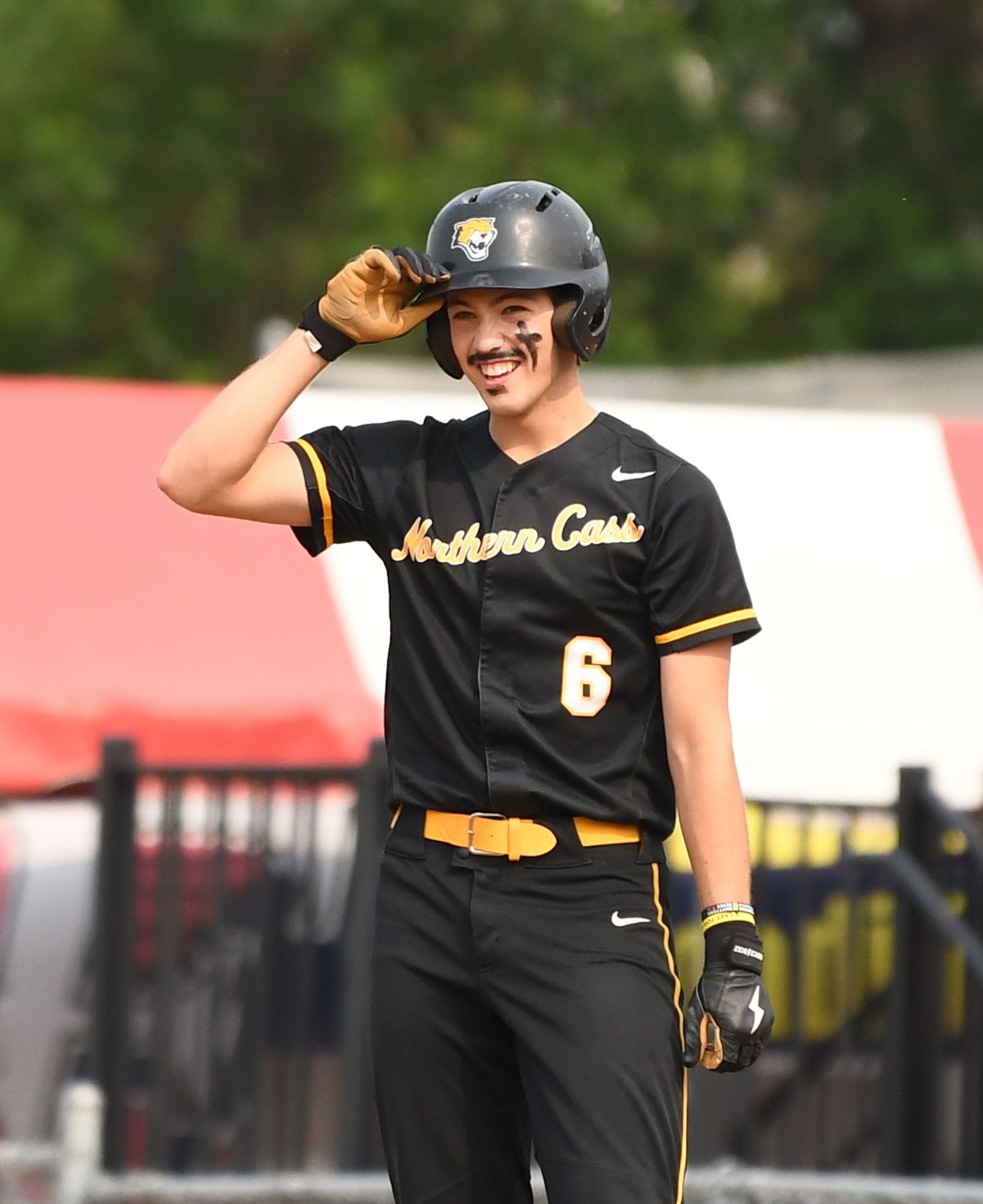 Baseball player in black and gold uniform smiles while adjusting helmet during game.