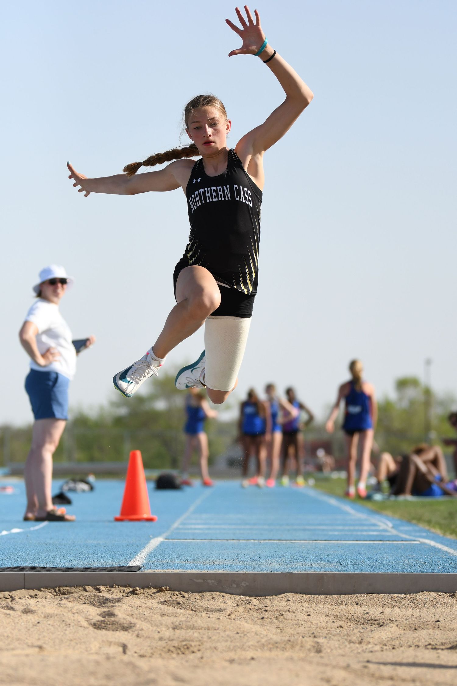 Track athlete soars through the air during long jump event at outdoor meet.