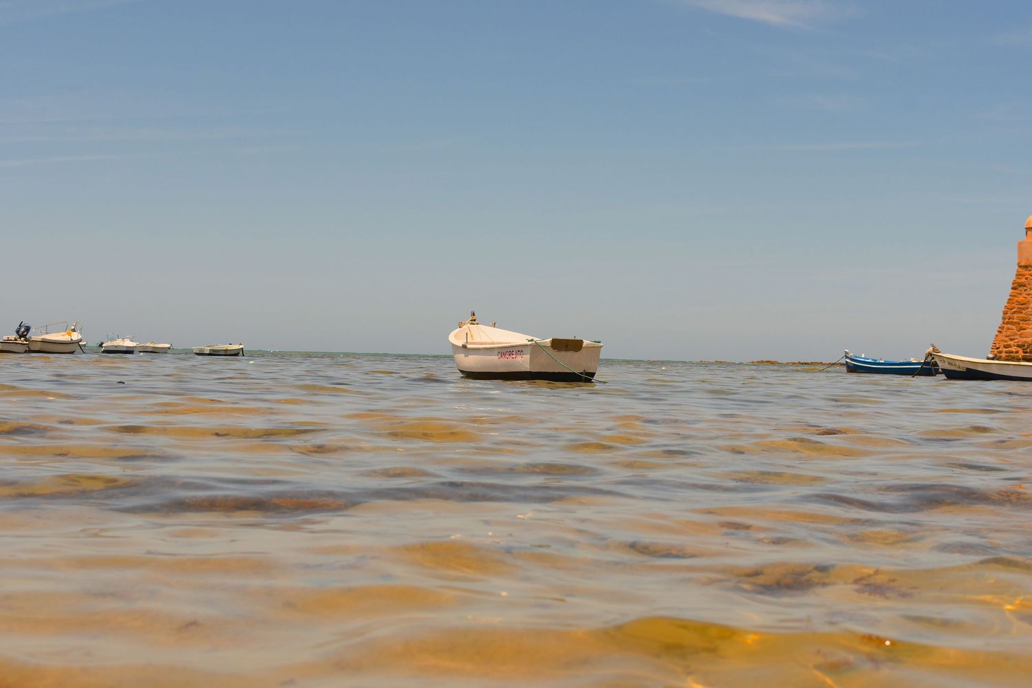 Small boats floating on brown waters under clear blue sky.