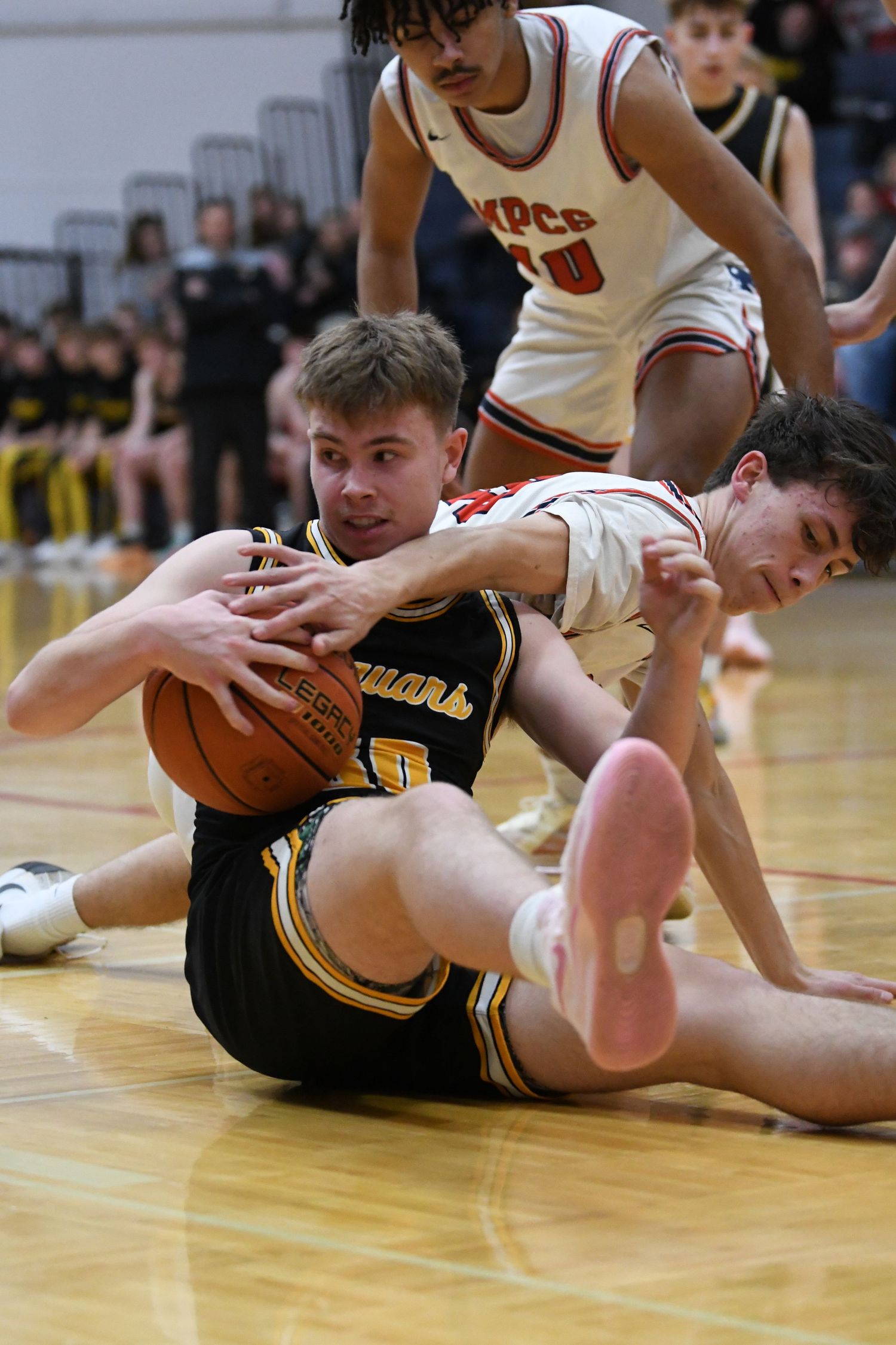 Players scramble for loose basketball on gymnasium floor during intense game action.