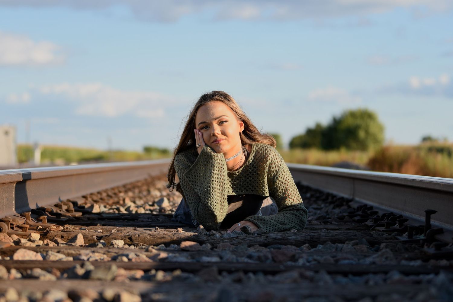 Silhouette of a person lying and posing on railroad tracks at sunset with warm golden lighting.
