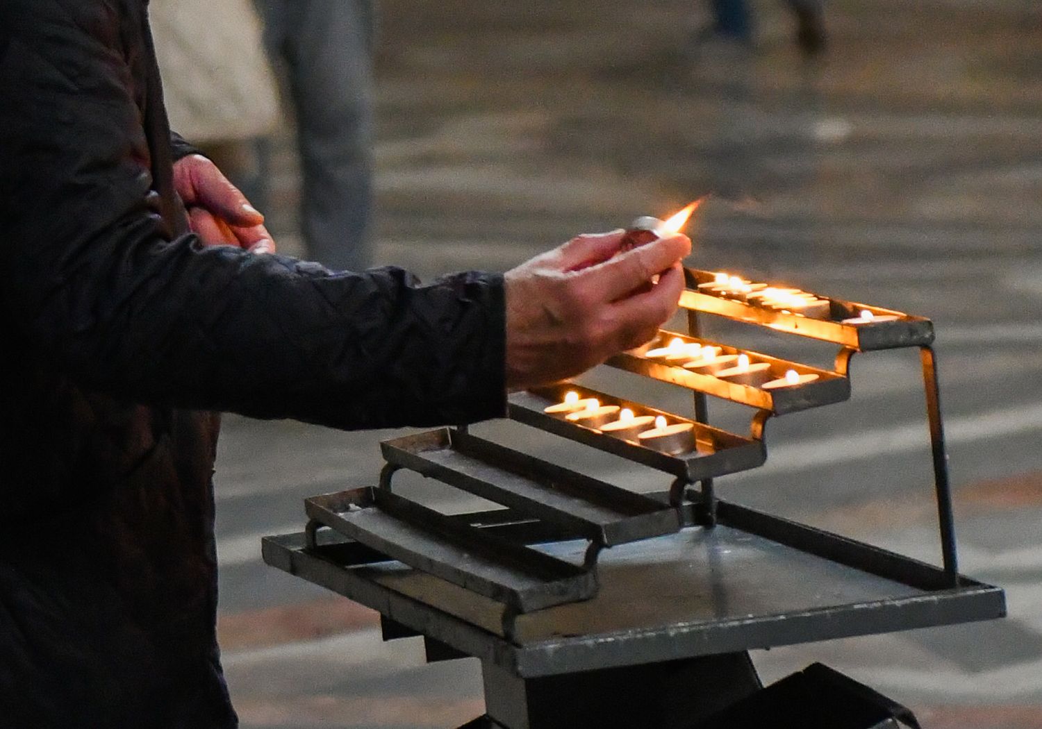 Person lighting votive candles on a metal stand in a dimly lit church interior.