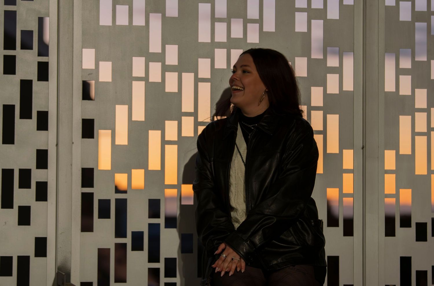 A silhouetted figure stands against a geometric patterned wall with warm sunset lighting.