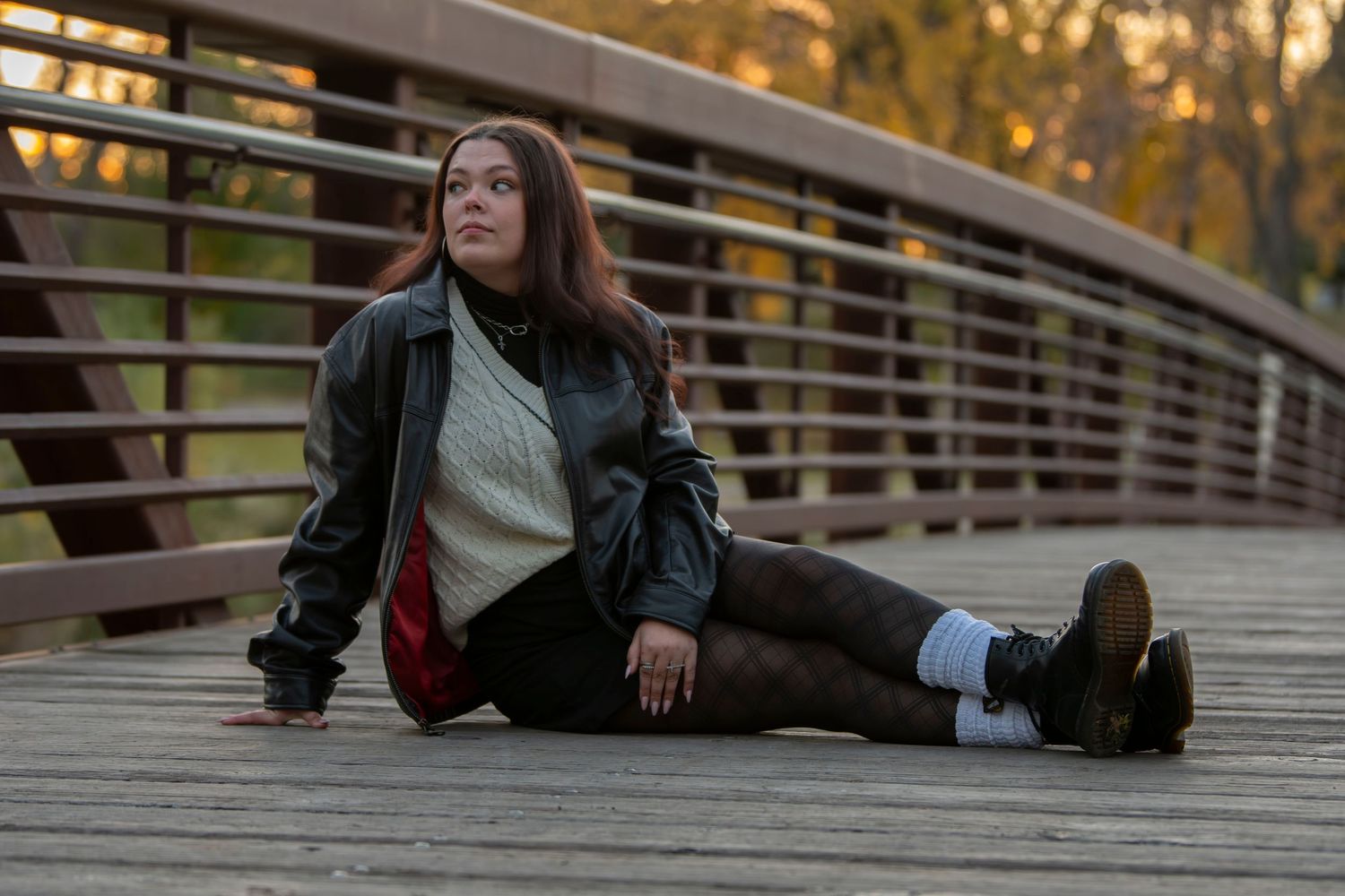 Person in casual attire sits on wooden bridge railing during golden sunset hour.