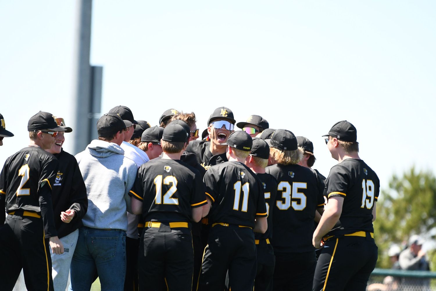 Baseball team huddles together on the field wearing black uniforms with yellow accents.