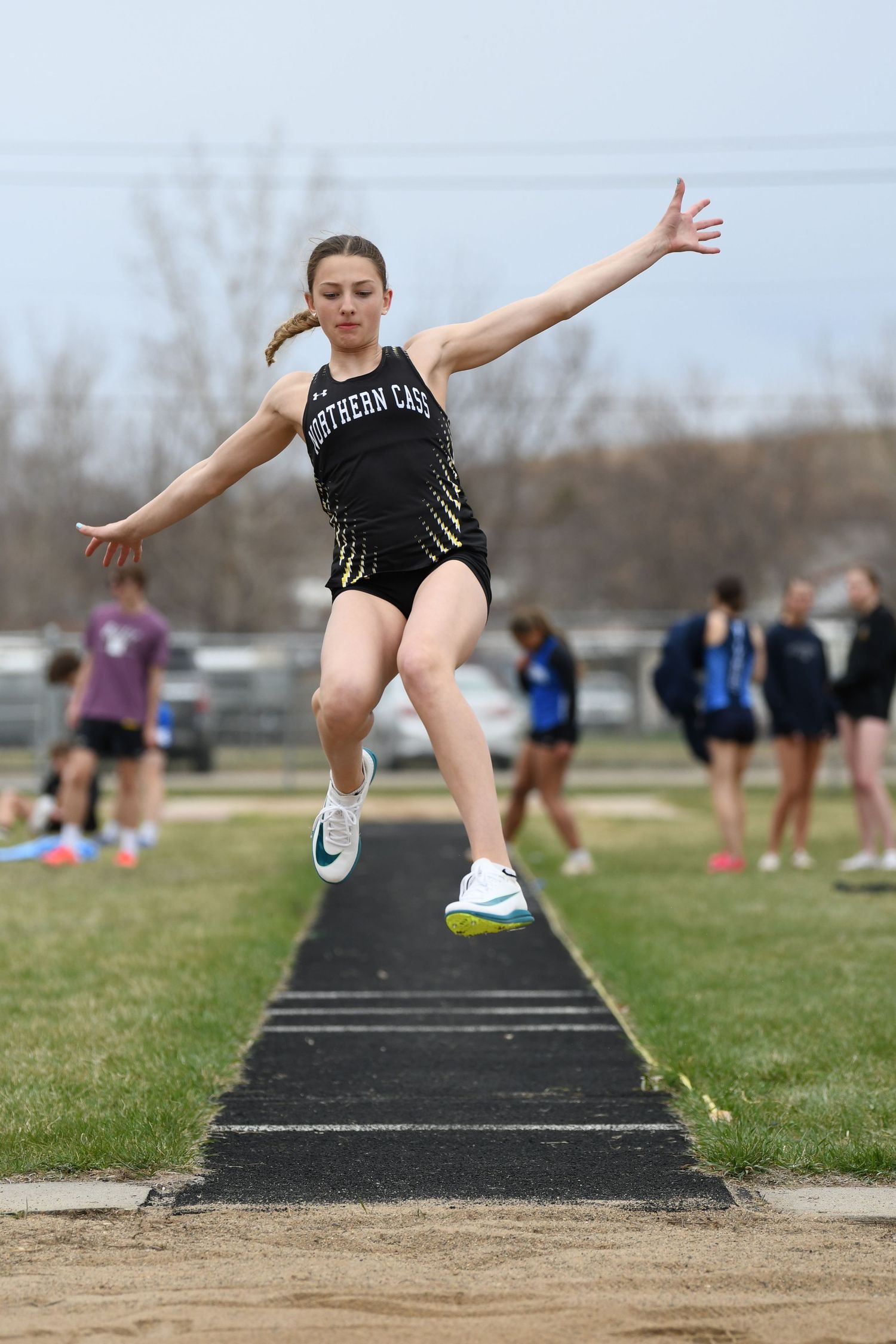 Track athlete performs dynamic long jump at outdoor competition.