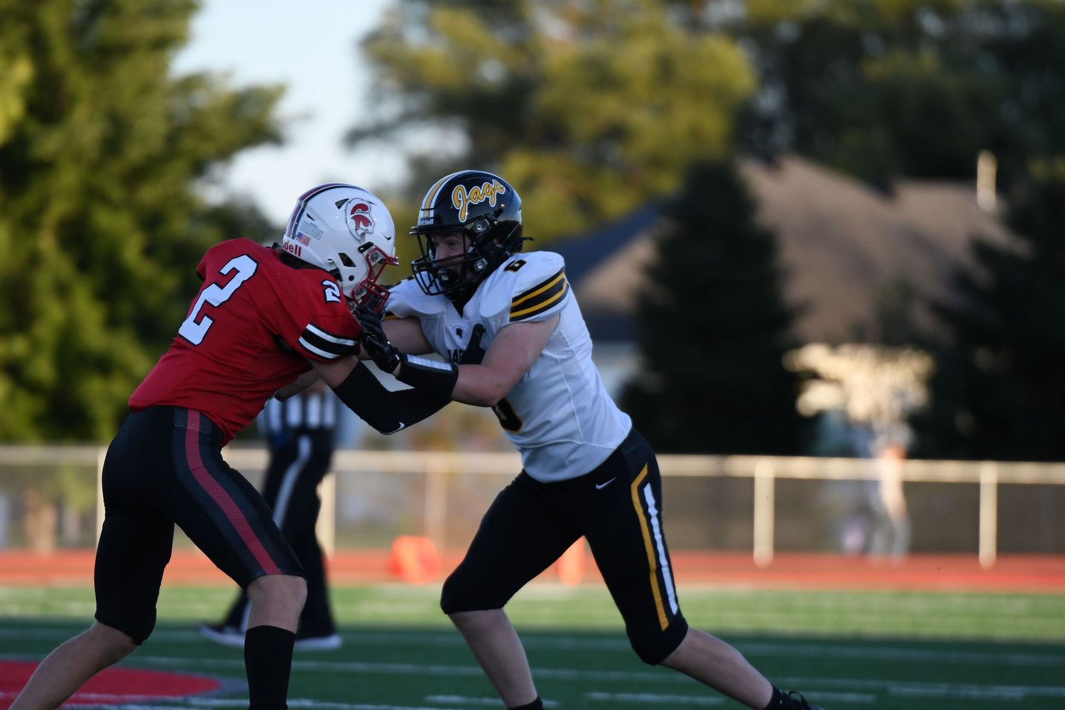 Football players collide during competitive tackle on grass field at sunset.