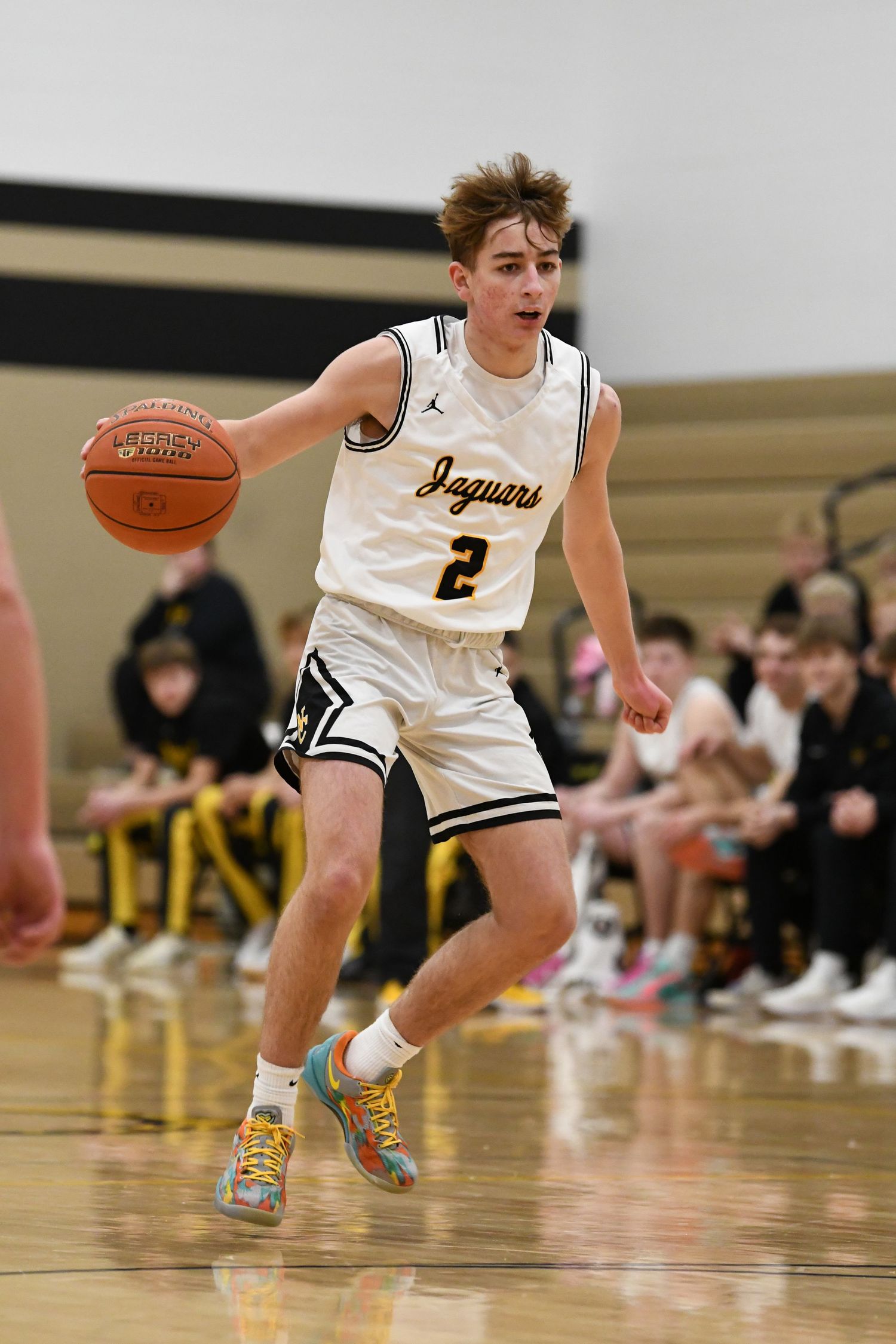Basketball player in white Jaguars jersey dribbles on court during game action.