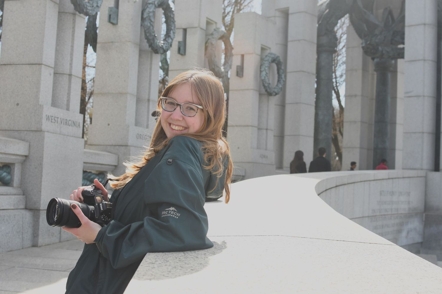 A photographer with a camera poses near classical architecture columns.