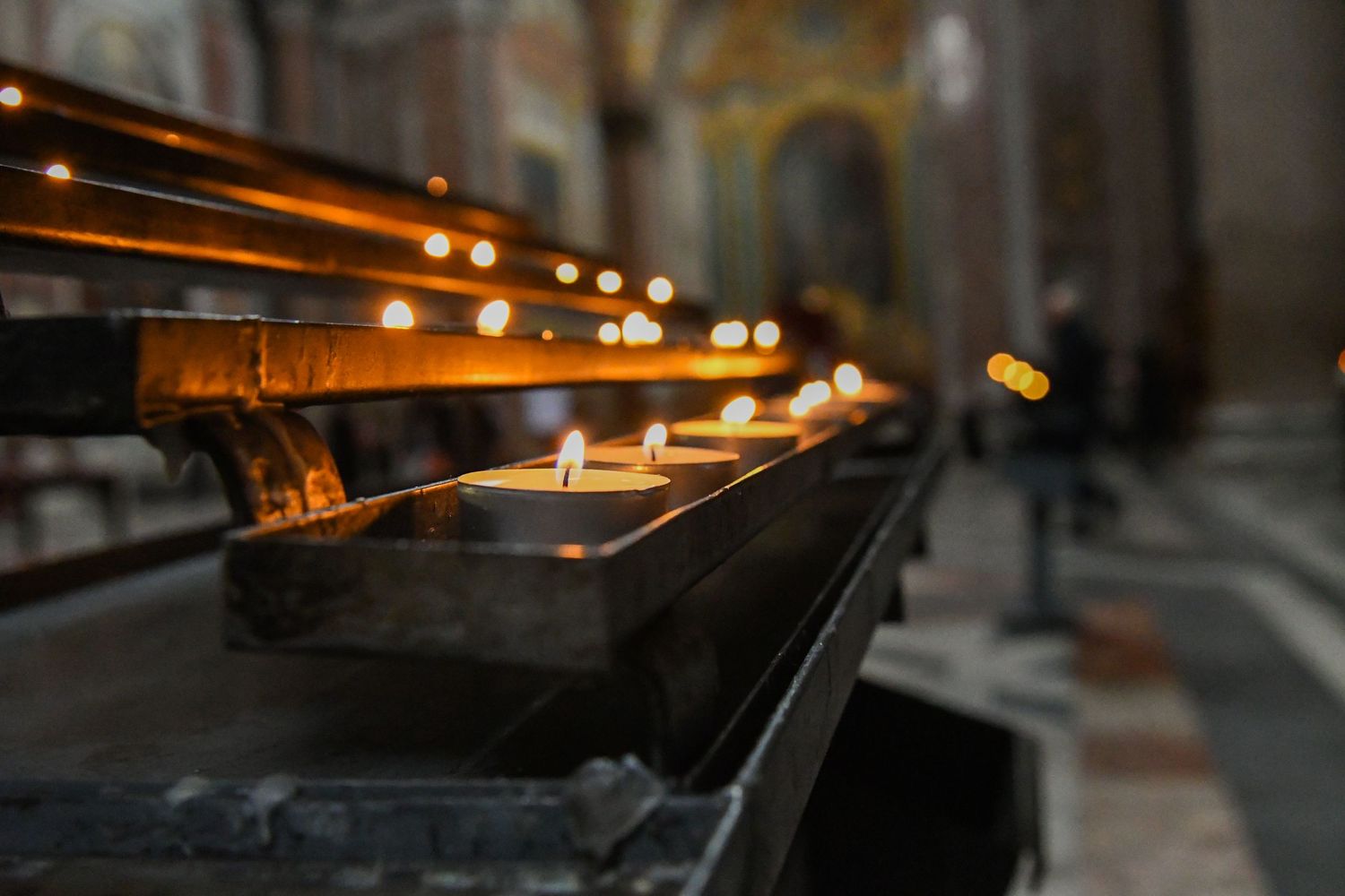 Row of glowing votive candles creating atmospheric lighting in a historic church interior.
