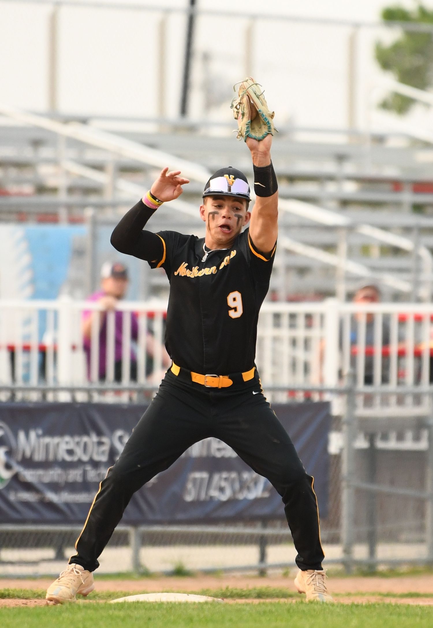 Baseball player in black uniform reaches up to make defensive play during game.