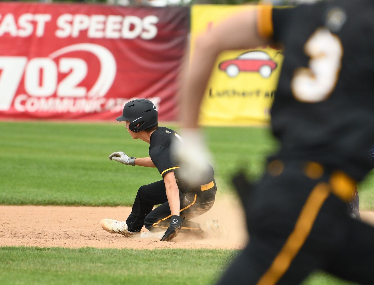 Baseball player in black uniform slides into base during competitive game action.