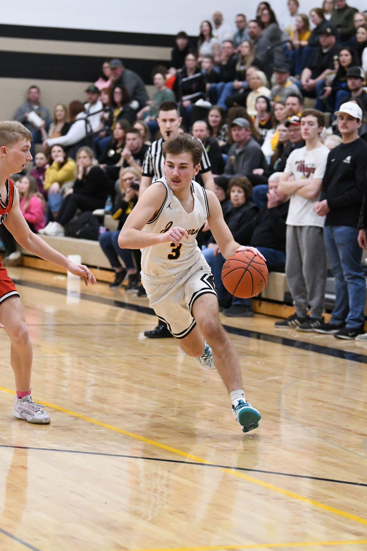 Player in white jersey drives baseline past defender during basketball game.