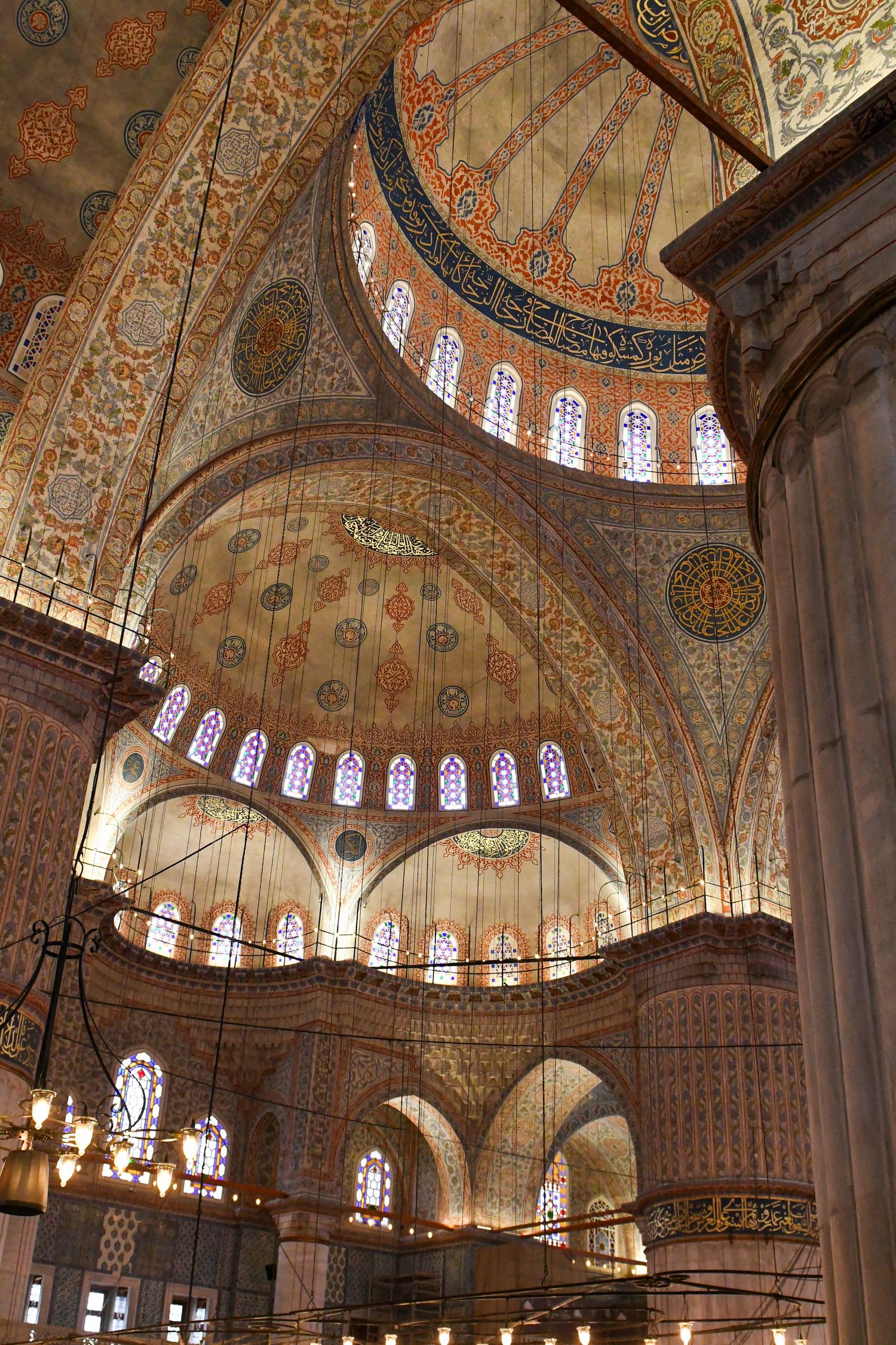 Ornate domed ceiling of a mosque with intricate Islamic patterns and stained glass windows.