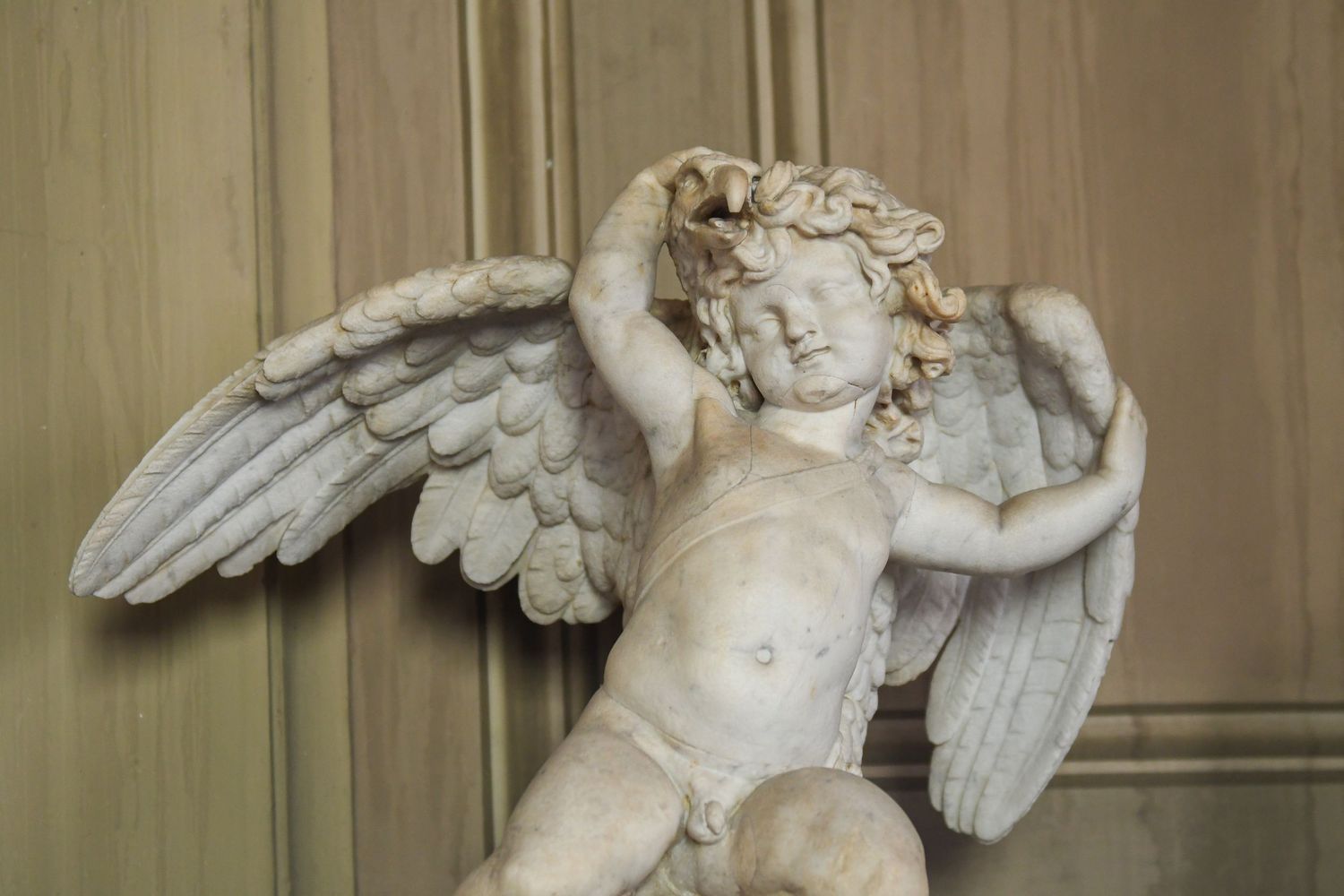 Classical marble sculpture of winged figures in museum setting.