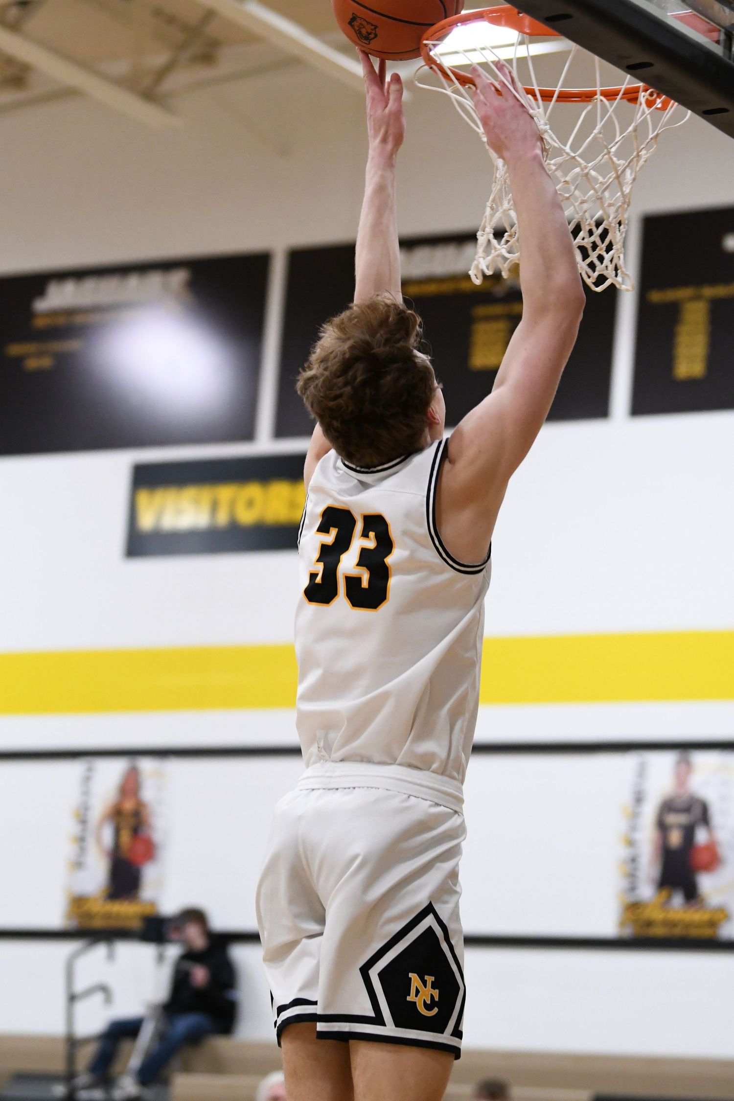 Basketball player in white uniform goes for a slam dunk during game.