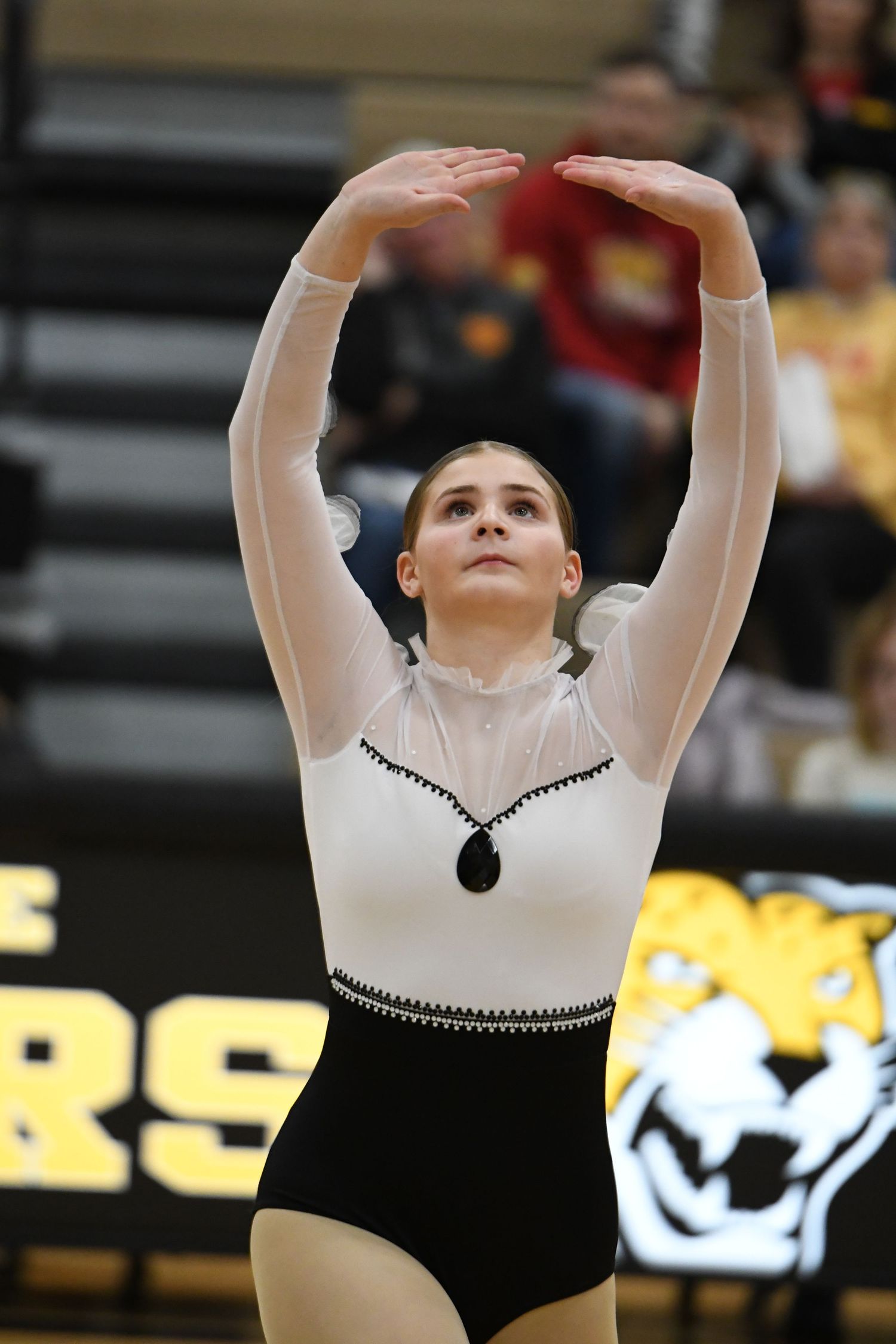 Dancer performs graceful arm movements in elegant black and white costume on gymnasium floor.
