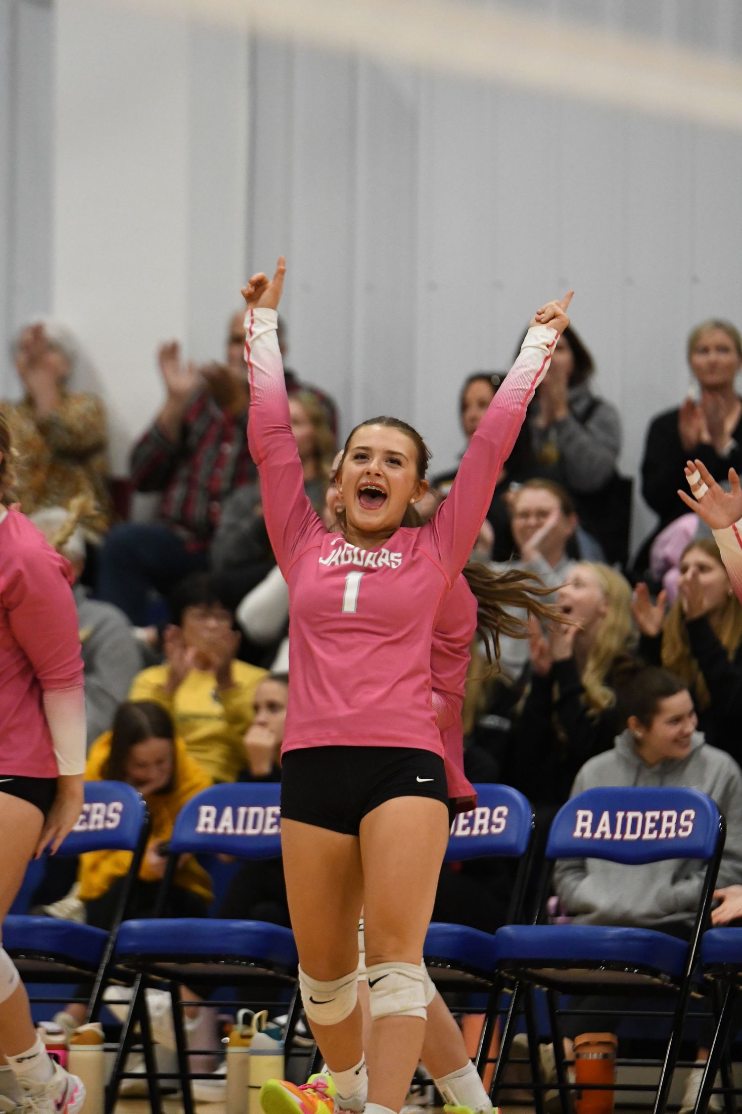 Players in pink jerseys celebrate enthusiastically from the sidelines during a volleyball game.