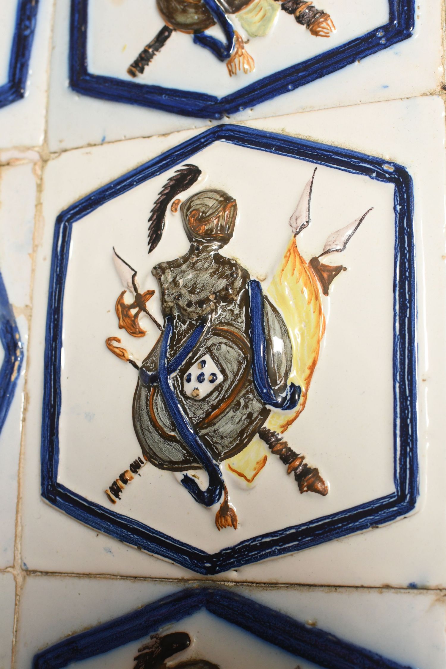 Medieval decorative tiles with blue hexagonal borders featuring painted figures holding torches and objects.