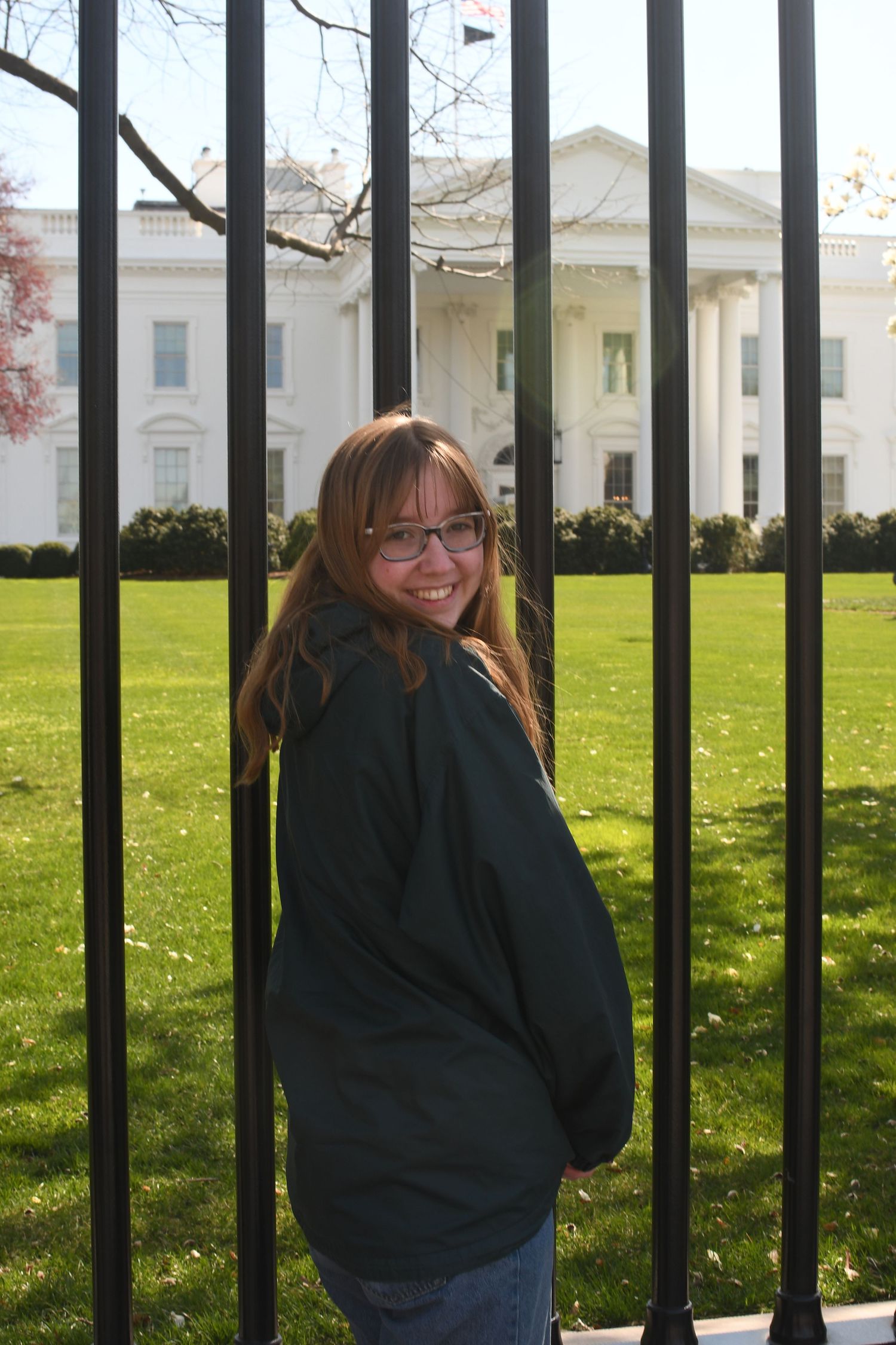 A photographer poses in front of the White House fence on a sunny day.