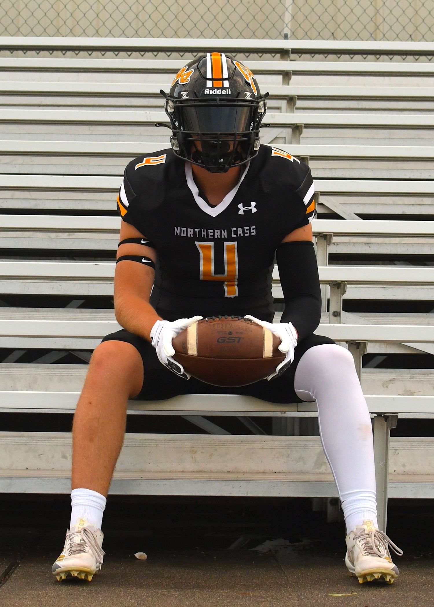 Football player in black and orange uniform sitting on bleachers holding ball.