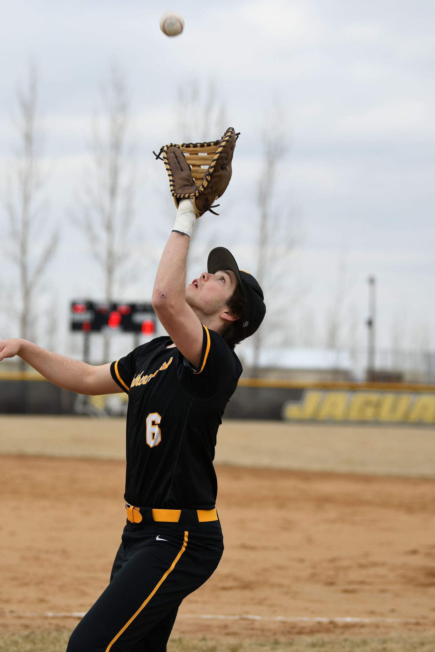 Baseball player reaches up to catch a pop fly ball during game.