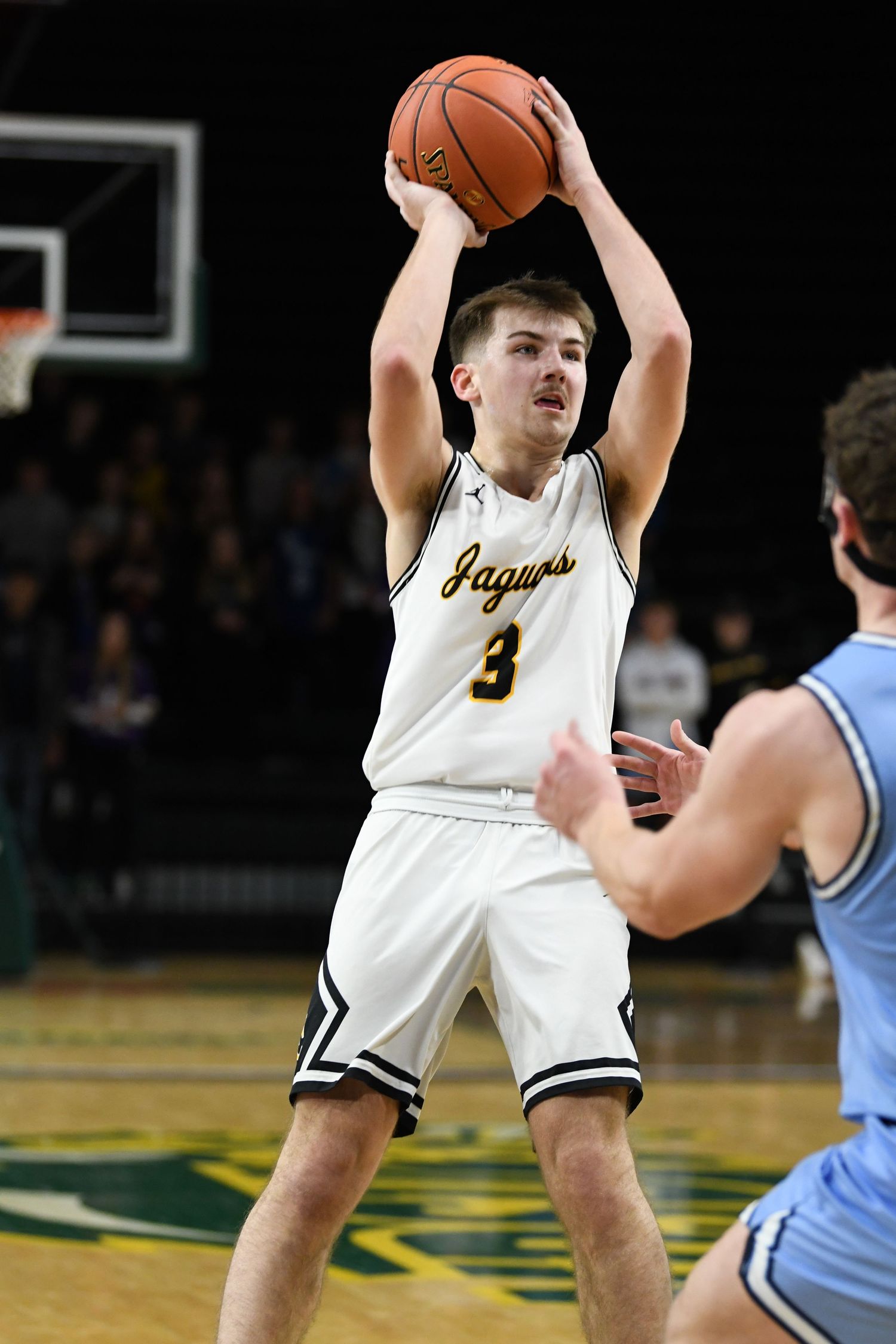 Basketball player in white jersey takes jump shot during game.