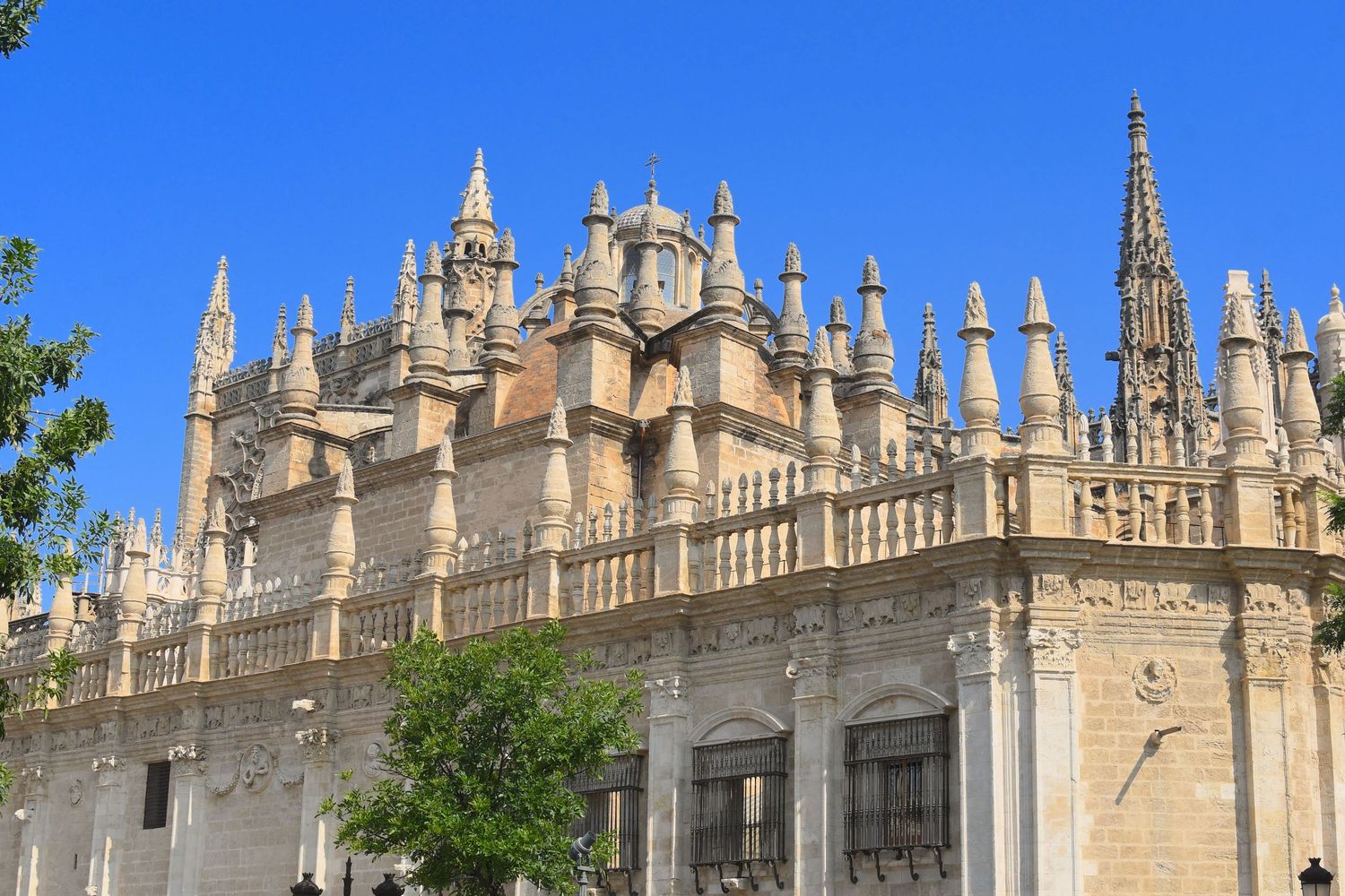 Gothic cathedral with ornate spires and detailed stonework against bright blue sky in Seville, Spain.