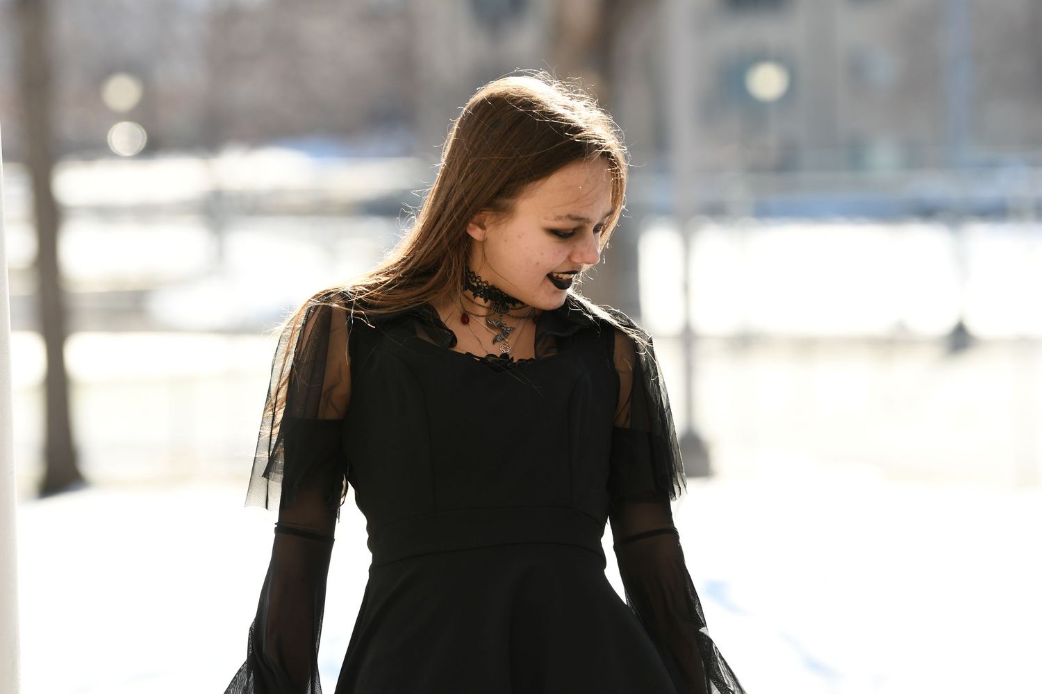 Woman in an elegant black dress poses outdoors in a winter setting.