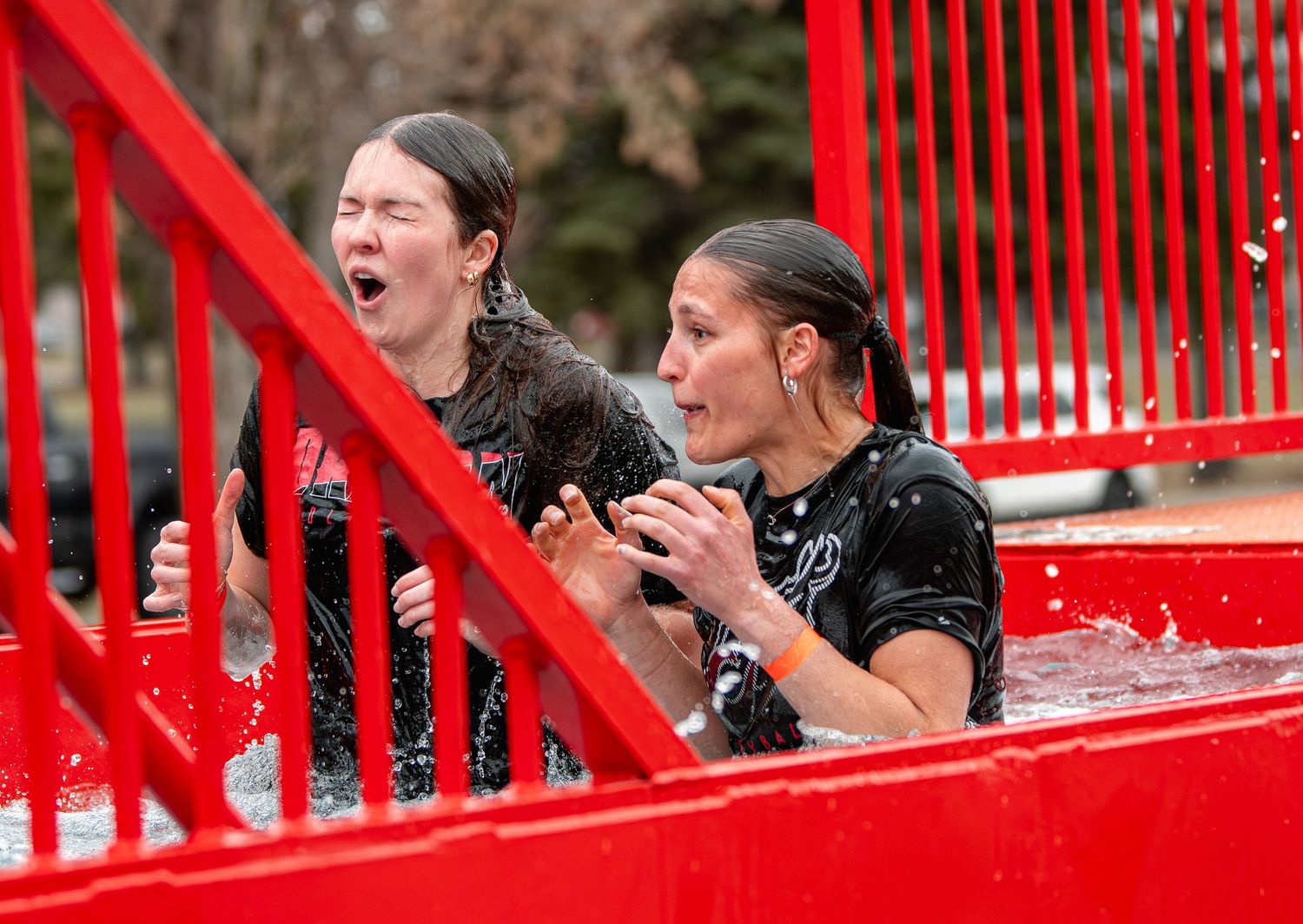Two women react with shock and excitement while submerged in cold water during a polar plunge event.
